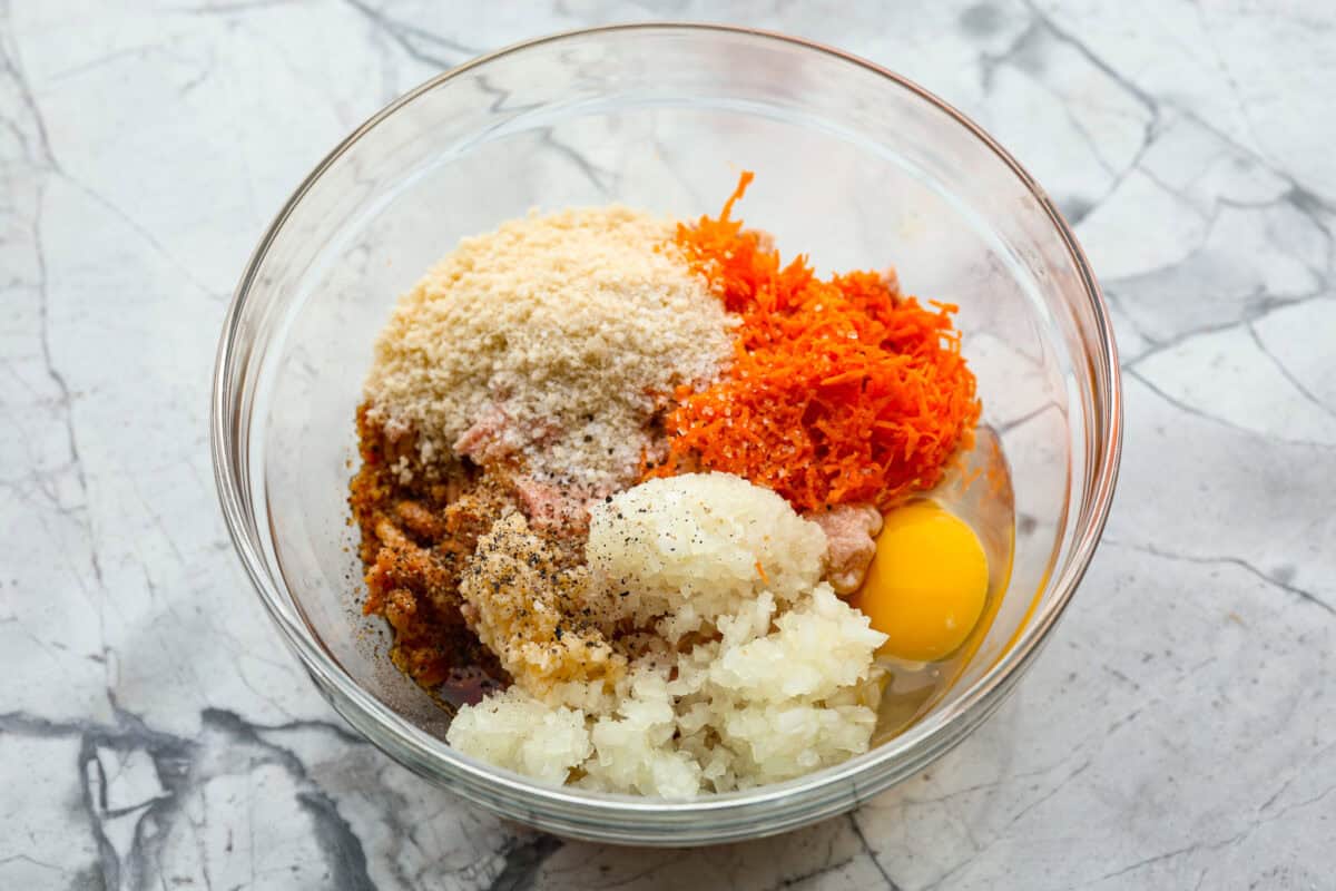 Easy Bola Bola (Filipino meatballs) combine pork, panko breadcrumbs, carrots, and onions to create a versatile meatball recipe. Tender and tasty on the inside then deep-fried and crispy on the outside! The perfect appetizer or dinner idea! First photo of the meatball ingredients added to a bowl.