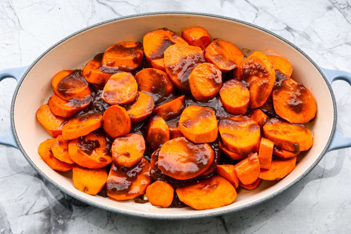 Baked candied yams are one of my favorite Thanksgiving side dishes. The succulent potato texture mixed with the sweet brown sugar spiced sauce, baked to candy perfection, tastes incredible. Overhead shot of sliced yams with sugar and butter mixture spread over the top.