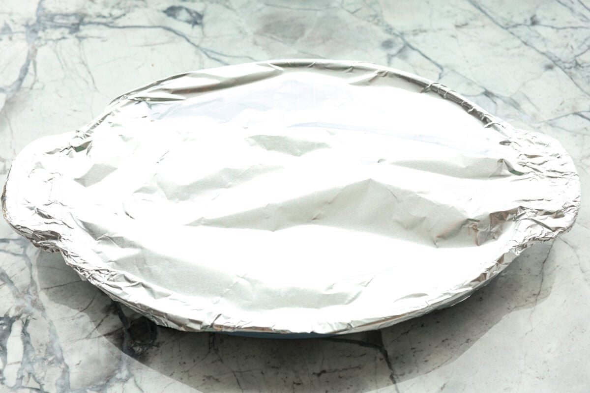 Baked candied yams are one of my favorite Thanksgiving side dishes. The succulent potato texture mixed with the sweet brown sugar spiced sauce, baked to candy perfection, tastes incredible. Overhead shot of baking dish with yams and sauce covered with tinfoil.