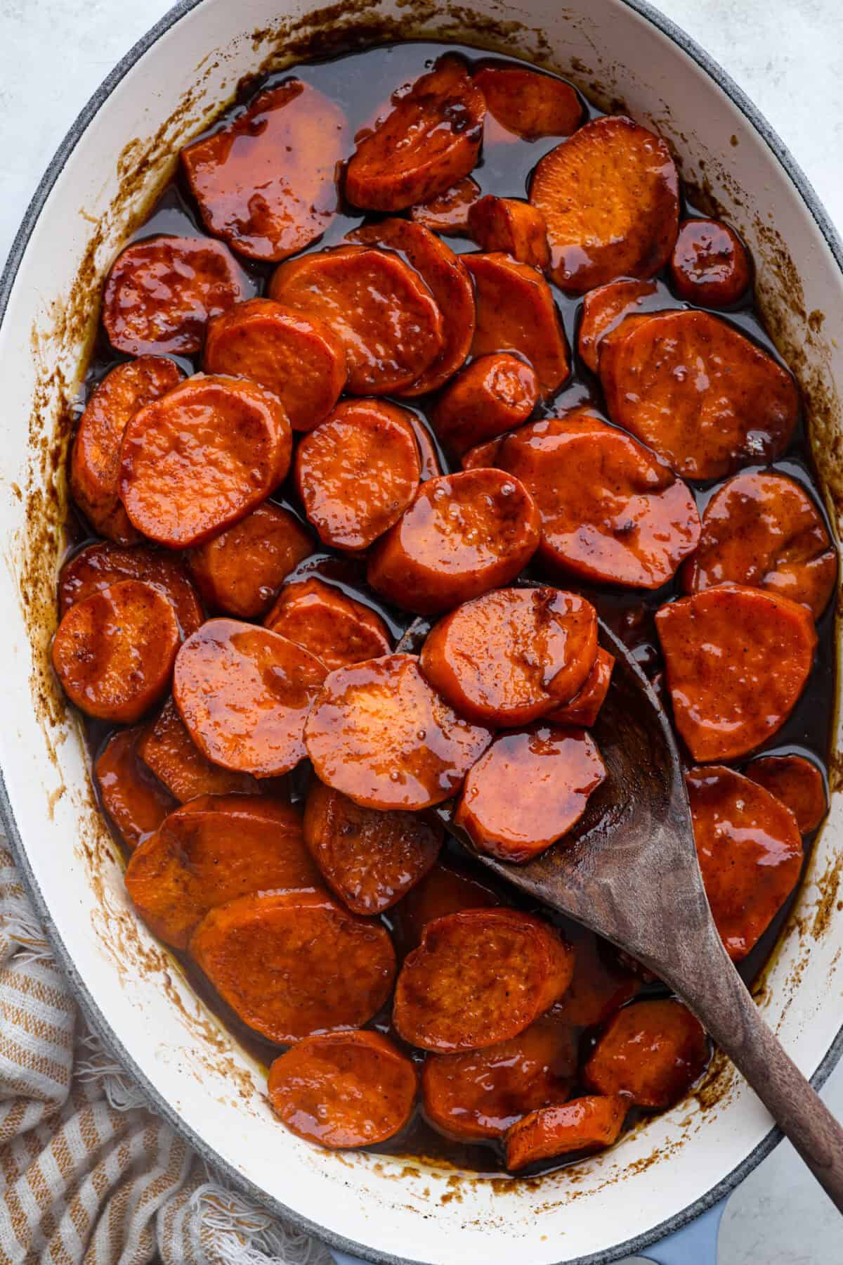 Baked candied yams are one of my favorite Thanksgiving side dishes. The succulent potato texture mixed with the sweet brown sugar spiced sauce, baked to candy perfection, tastes incredible. Overhead shot of baked candied yams in a baking dish with a wooden serving spoon.