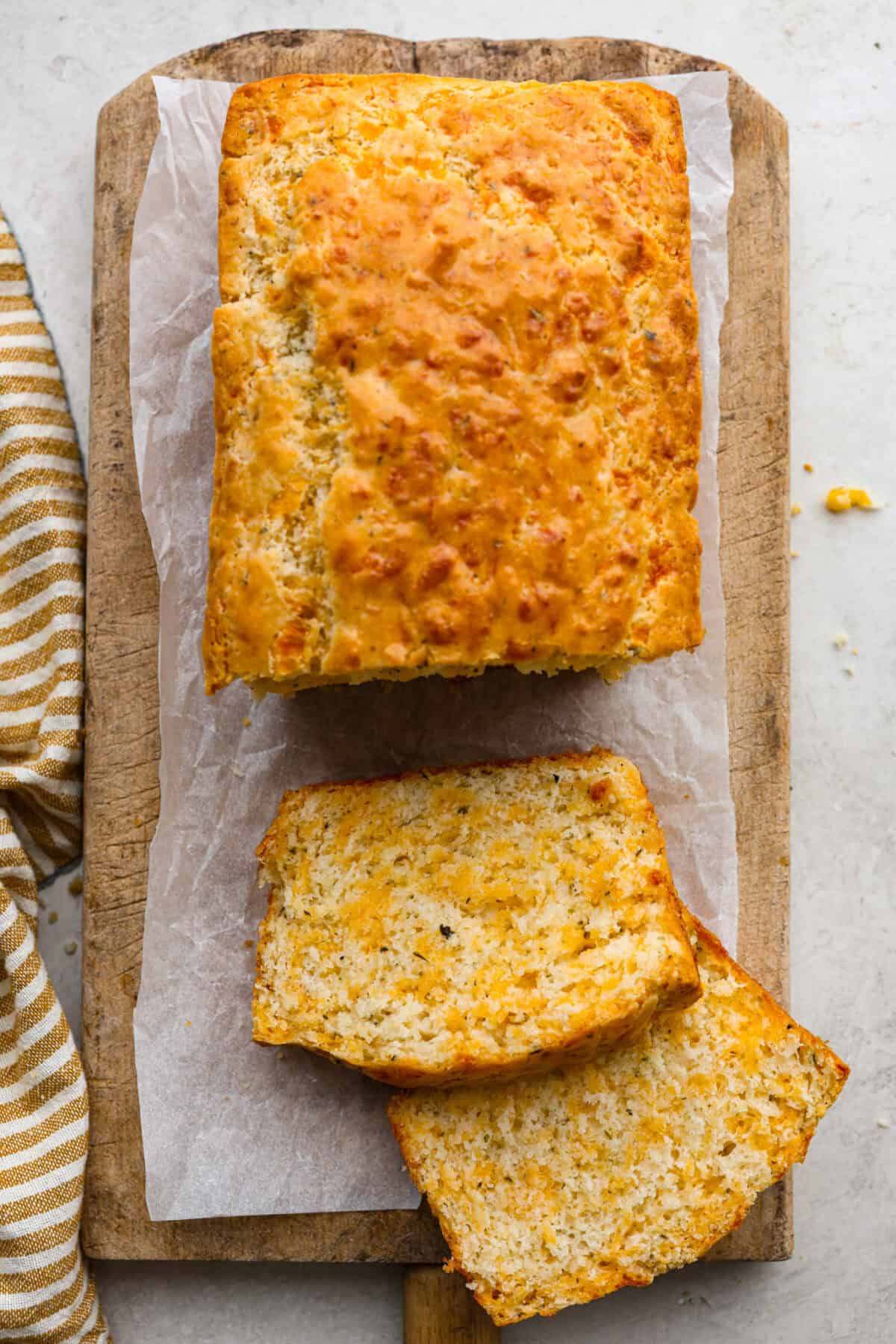 Easy Cheesy Quick Bread is packed with flavor and has a tender, golden crust and soft, moist interior. It's perfect with soup, salad, chili, or on its ownย with a pat of butter. It's simple to make and irresistibly delicious! Overhead shot of loaf of cheesy quick bread with a couple pieces cute from it.