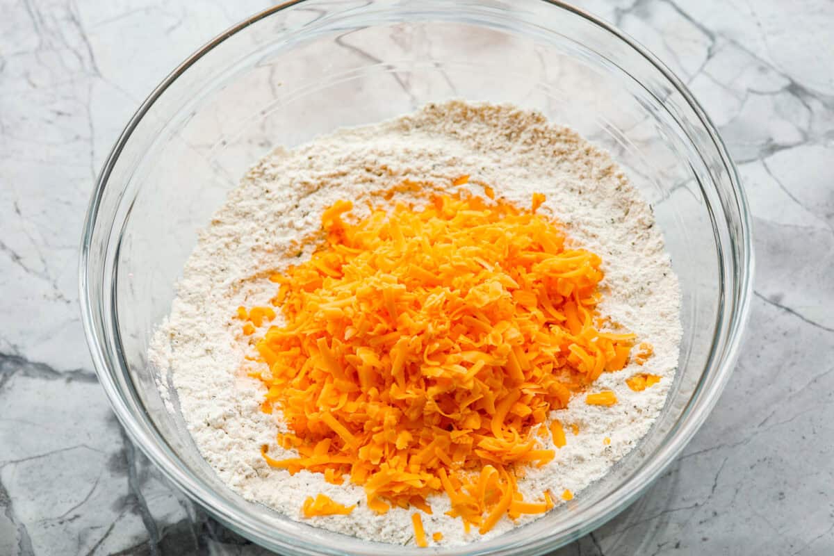 Easy Cheesy Quick Bread is packed with flavor and has a tender, golden crust and soft, moist interior. It's perfect with soup, salad, chili, or on its ownย with a pat of butter. It's simple to make and irresistibly delicious! Overhead shot of cheese added to the dry ingredients.