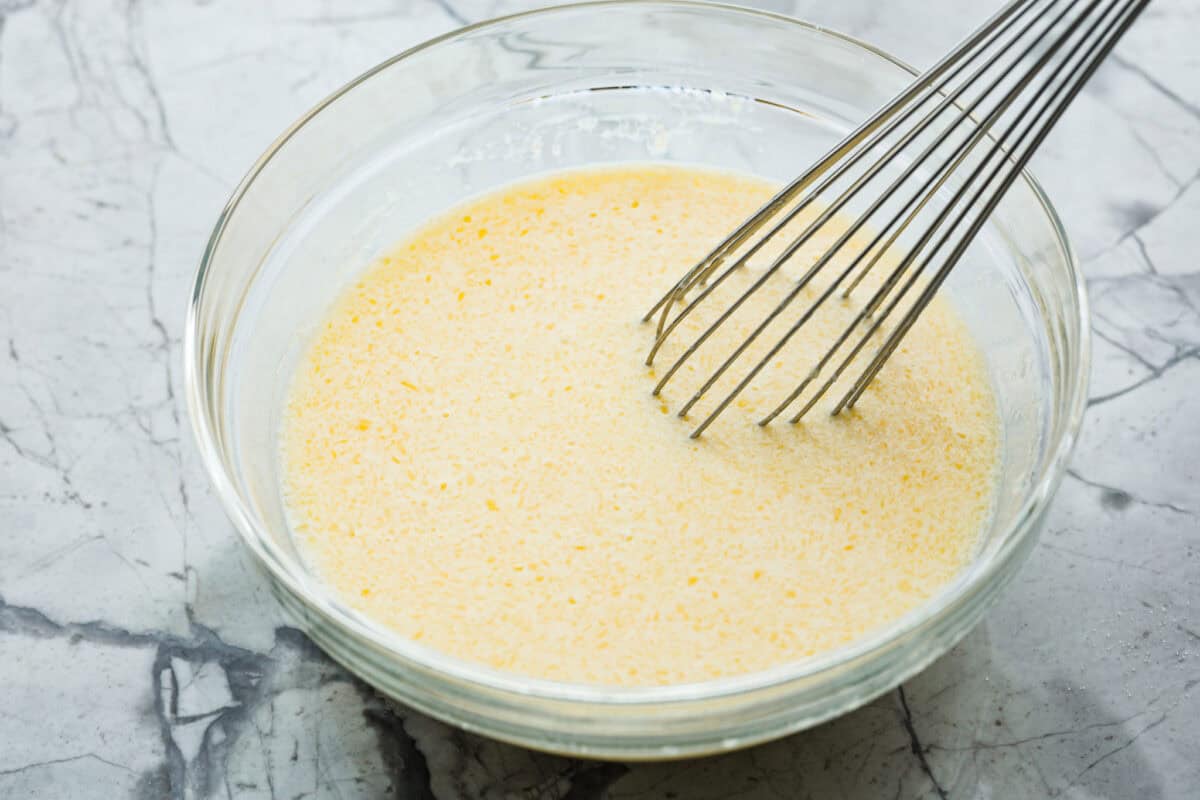 Easy Cheesy Quick Bread is packed with flavor and has a tender, golden crust and soft, moist interior. It's perfect with soup, salad, chili, or on its ownย with a pat of butter. It's simple to make and irresistibly delicious! Angle shot of eggs, milk and melted butter whisked together in a bowl.