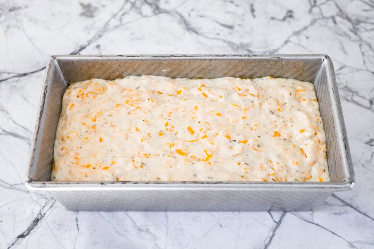 Easy Cheesy Quick Bread is packed with flavor and has a tender, golden crust and soft, moist interior. It's perfect with soup, salad, chili, or on its ownย with a pat of butter. It's simple to make and irresistibly delicious! Angle shot of bread batter in the bread pan.