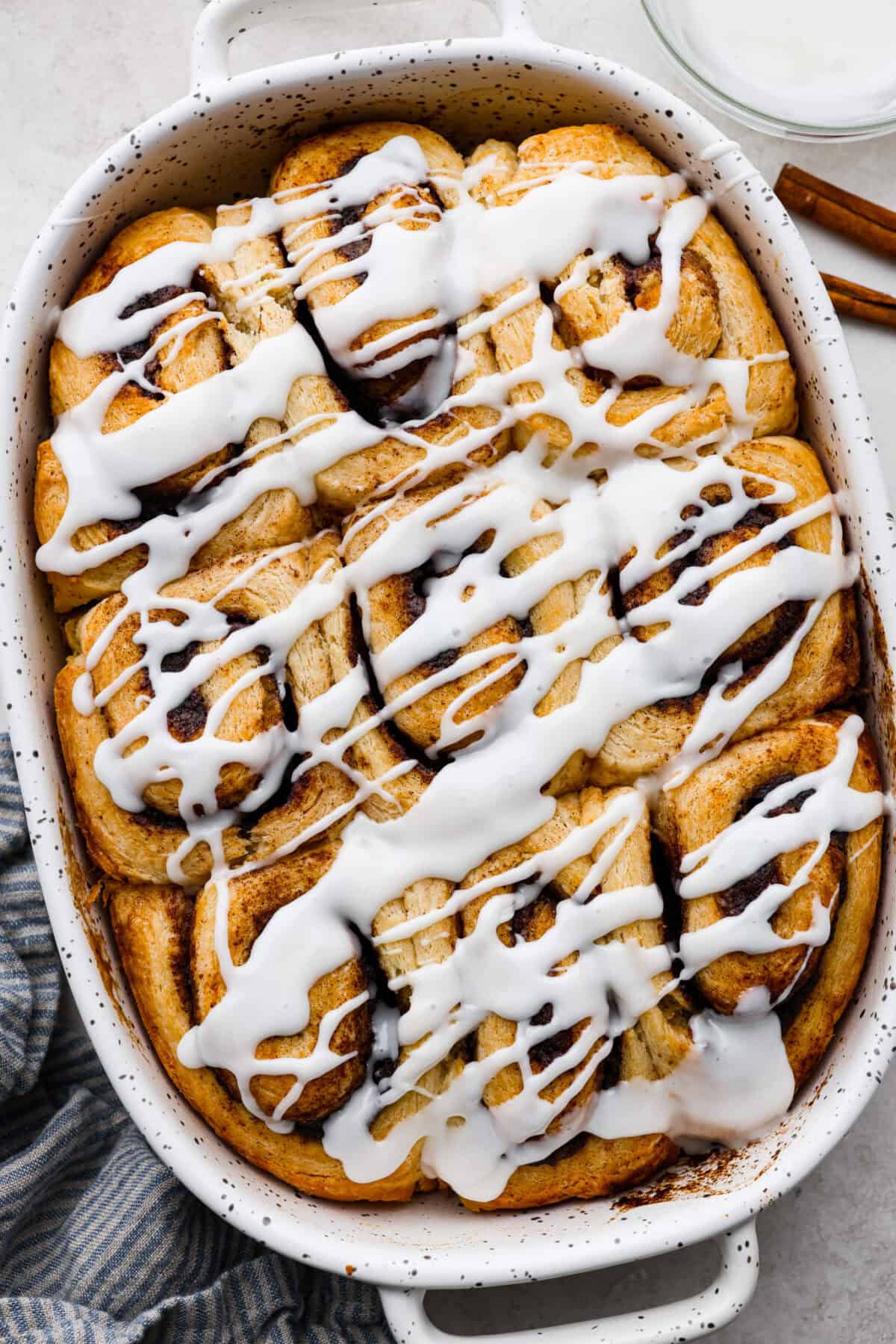 Biscuit Cinnamon Rolls are the most amazing twist on a classic! They are perfectly light, fluffy, and packed with cinnamon. The texture is more flakey and moist than traditional cinnamon rolls! Whether it’s for a cozy weekend breakfast or a holiday brunch, these hit the spot! Overhead shot of biscuit cinnamon rolls in a baking dish drizzled with glaze.