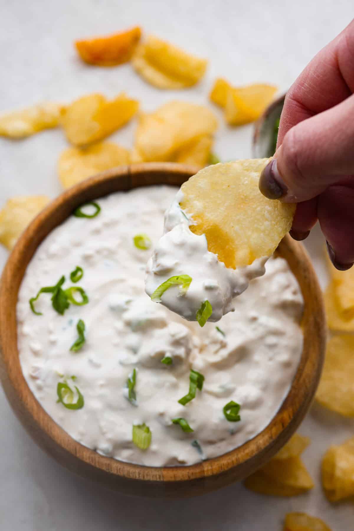 This clam dip is creamy, savory and the ultimate crowd-pleaser for any gathering! Whether paired with crispy chips or fresh veggies, it’s a quick and easy recipe that tastes incredible. Perfect for game day, potlucks, holidays or a casual snack! Overhead shot of someone sipping a chip into the clam dip.