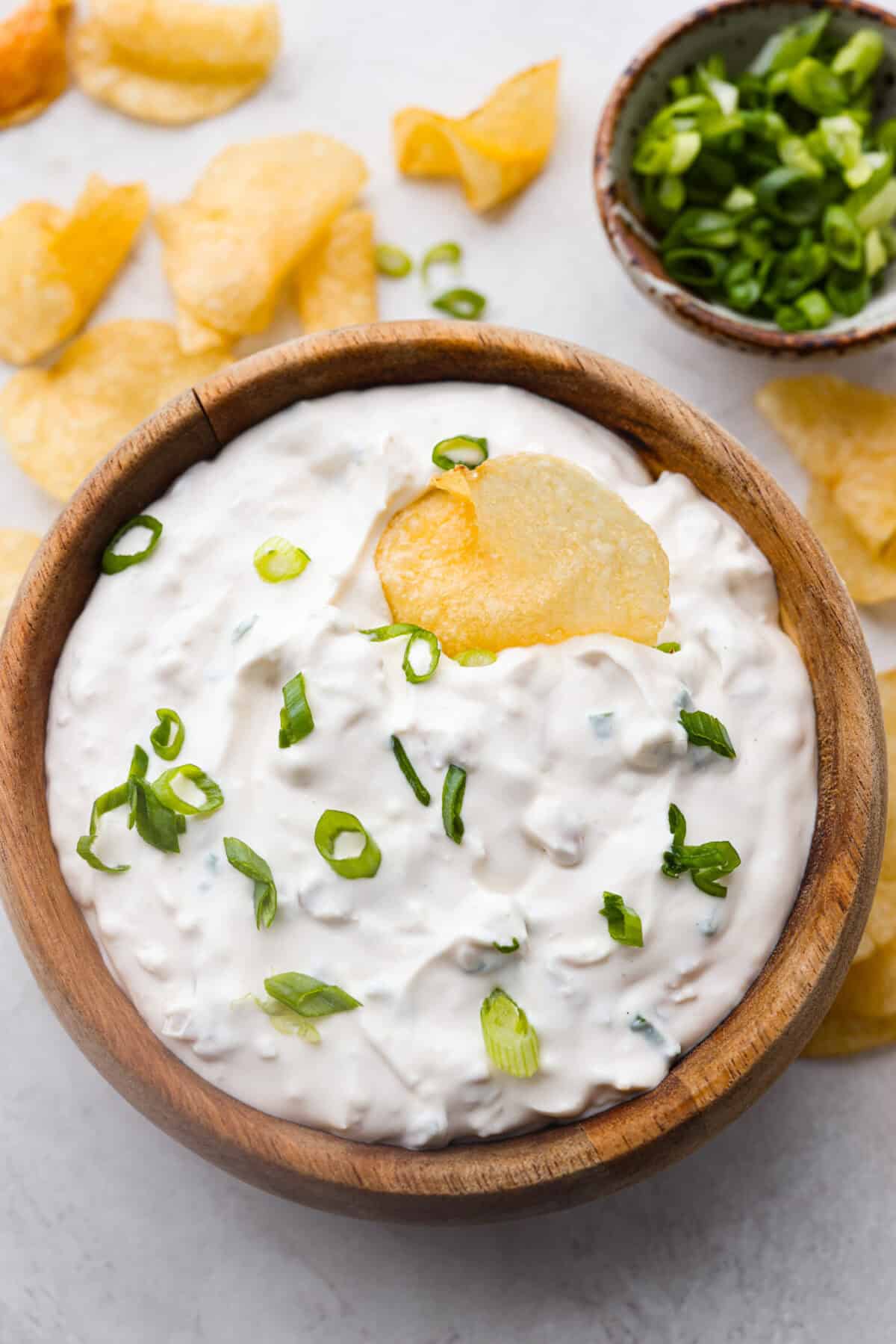 This clam dip is creamy, savory and the ultimate crowd-pleaser for any gathering! Whether paired with crispy chips or fresh veggies, it’s a quick and easy recipe that tastes incredible. Perfect for game day, potlucks, holidays or a casual snack! Overhead shot of a wooden bowl with clam dip inside.