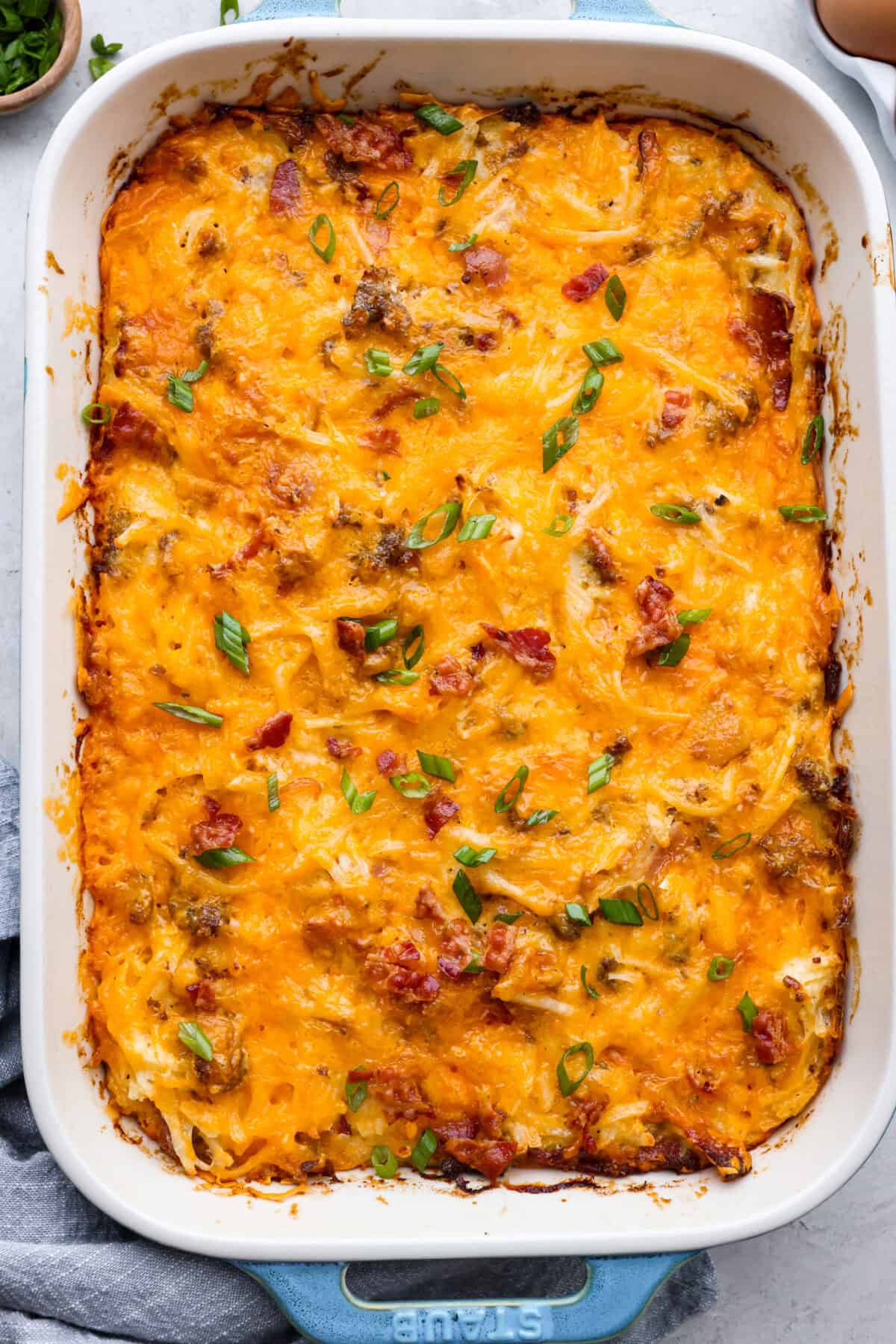 Crack breakfast casserole gets its name for a reason. It is bursting with delicious flavors you won't want to stop eating! It's packed with layers of shredded potatoes, crispy bacon, sausage, and smooth cream cheese, topped with a layer of crispy cheese. Overhead shot of crack breakfast casserole in a baking dish.