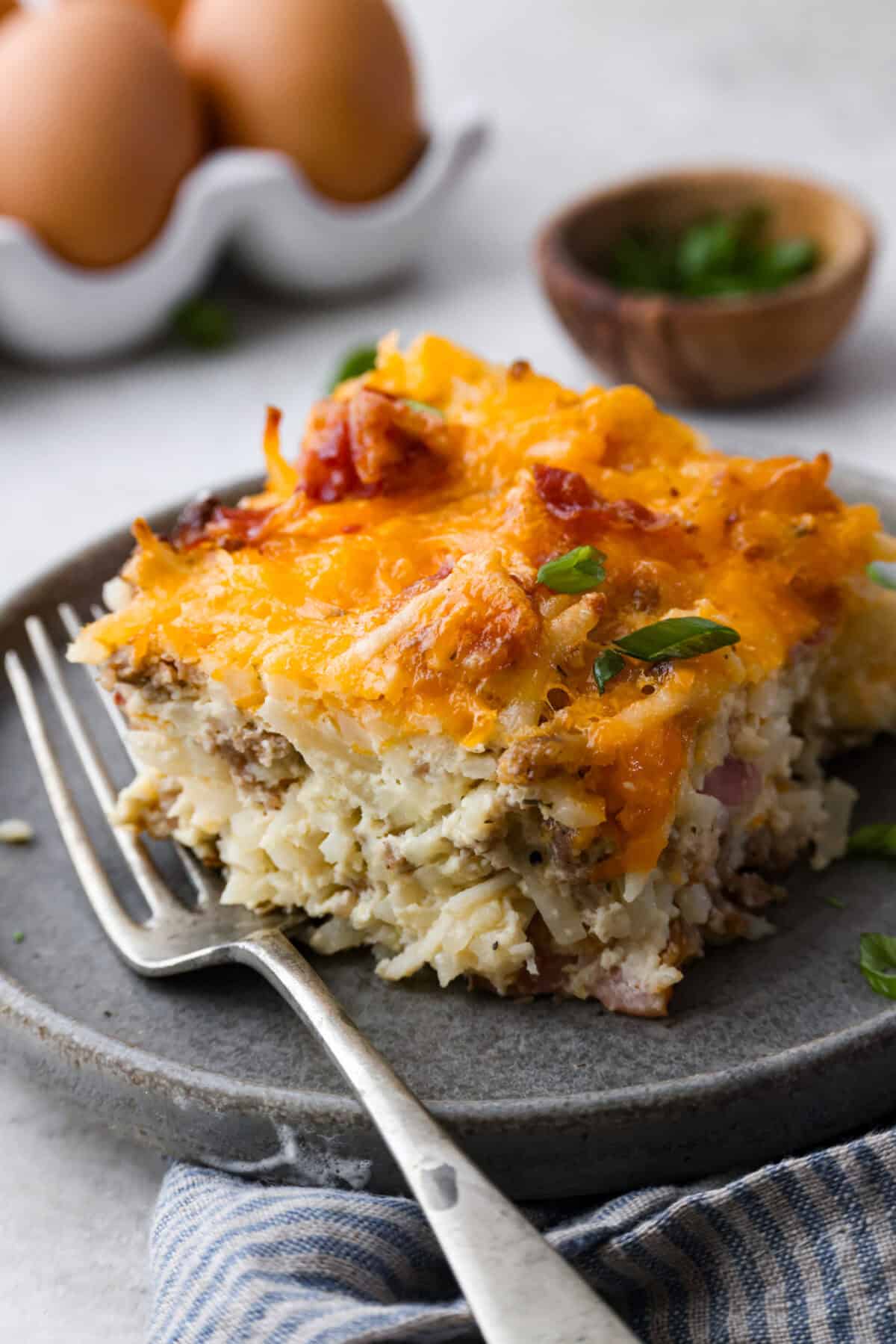 Crack breakfast casserole gets its name for a reason. It is bursting with delicious flavors you won't want to stop eating! It's packed with layers of shredded potatoes, crispy bacon, sausage, and smooth cream cheese, topped with a layer of crispy cheese. Close up shot of a plated portion of crack breakfast casserole.