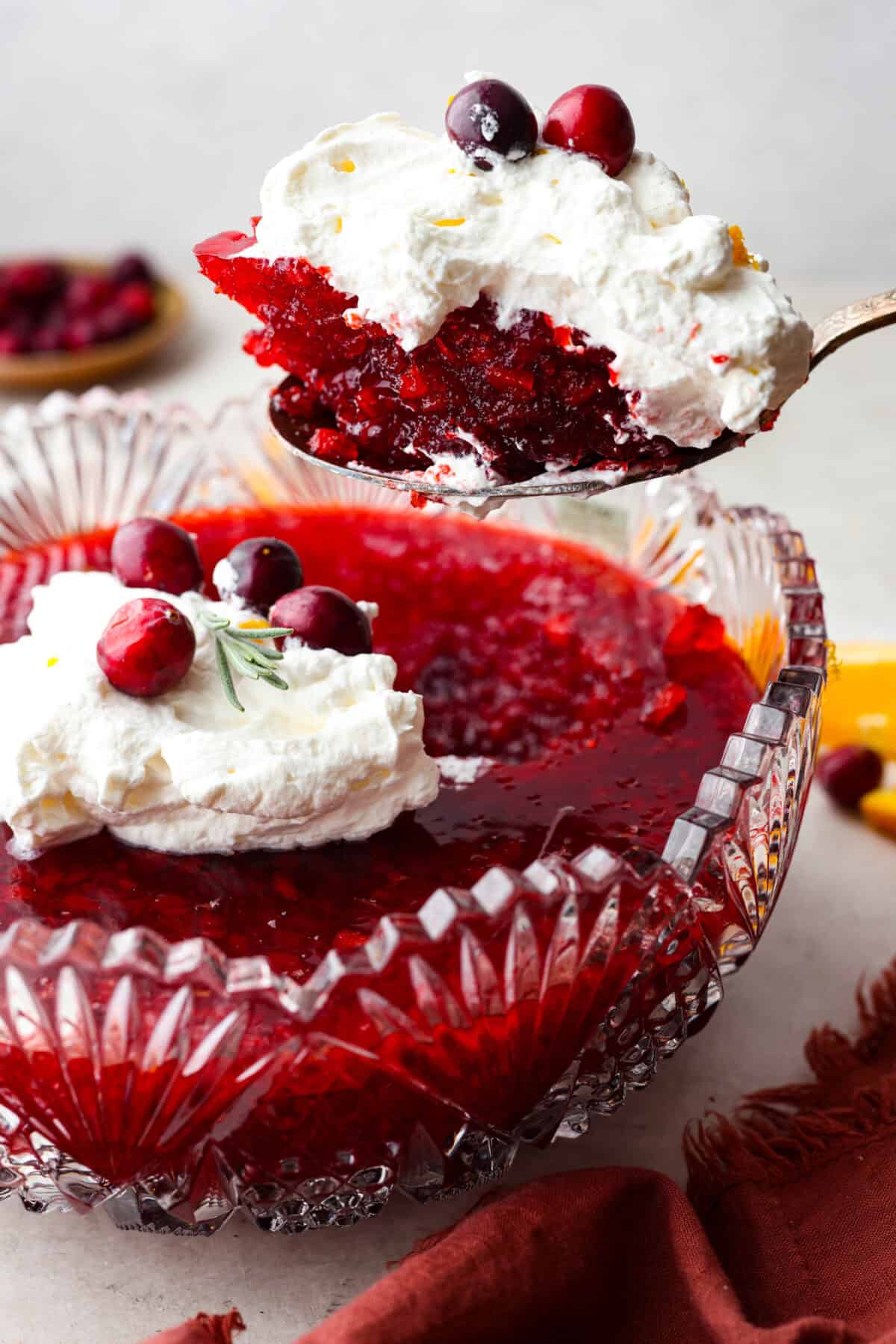 Cranberry Jello Salad is the best combination of tart, tangy, and sweet! It's similar to cranberry sauce but a little sweeter from the jello with undertones of orange and pineapple. Add it to your holiday spread and watch it disappear! Side shot of a scoop of cranberry jello salad being lifted out of the serving bowl.