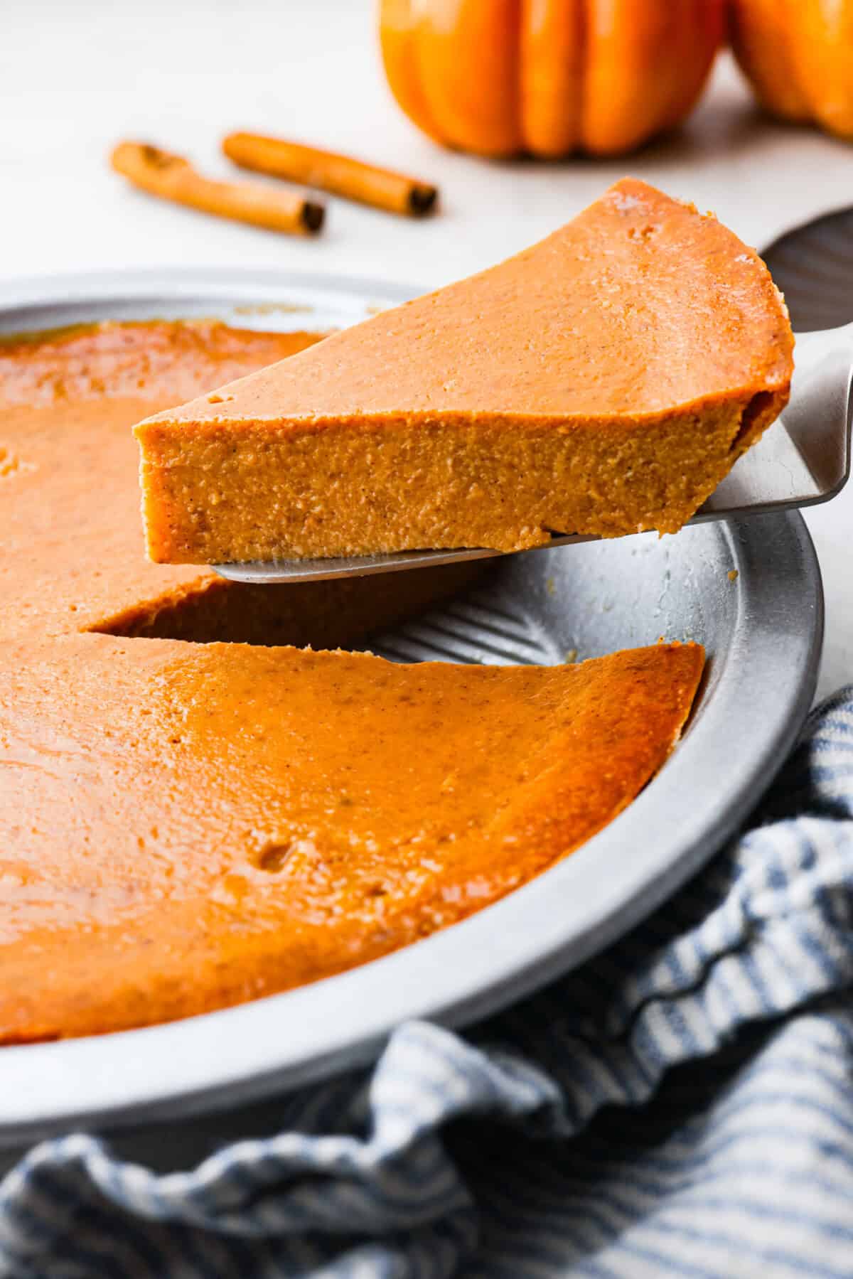 Crustless pumpkin pie has rich spices, creamy pumpkin, and a perfectly smooth texture. The custard holds its shape beautifully. Whether you're keeping things simple or exploring a gluten-free option, this pie gives all the nostalgic vibes of the classic. Angle shot of a slice of crustless pumpkin pie being lifted out the pie pan.