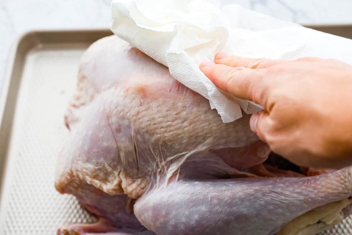 When you dry brine your turkey, you end up with a beautifully browned bird with crispy skin on the outside and juicy, flavorful meat on the inside! It will for sure be one of the most flavorful, moist turkeys you've ever had! Angle shot of someone patting the turkey dry with a paper towel.