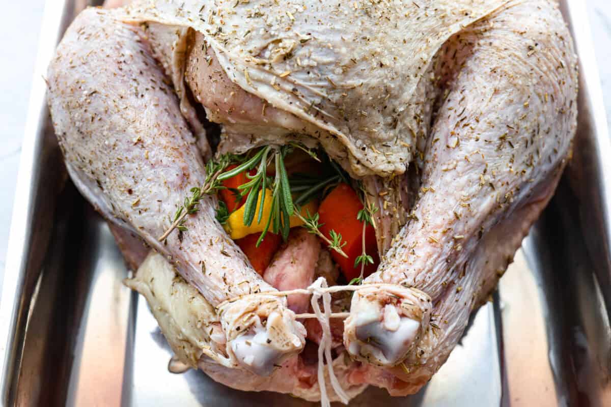 When you dry brine your turkey, you end up with a beautifully browned bird with crispy skin on the outside and juicy, flavorful meat on the inside! It will for sure be one of the most flavorful, moist turkeys you've ever had! Close up shot of the turkey covered in the seasoning mix, stuffed with lemon, carrots, onion and fresh herbs. The legs are tied together.
