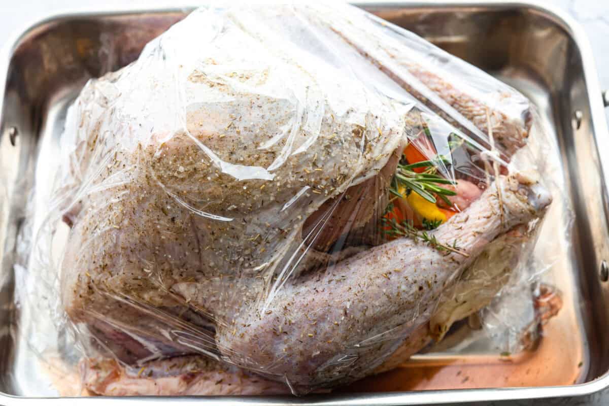 When you dry brine your turkey, you end up with a beautifully browned bird with crispy skin on the outside and juicy, flavorful meat on the inside! It will for sure be one of the most flavorful, moist turkeys you've ever had! Side shot of the prepared turkey covered in plastic wrap in a pan.