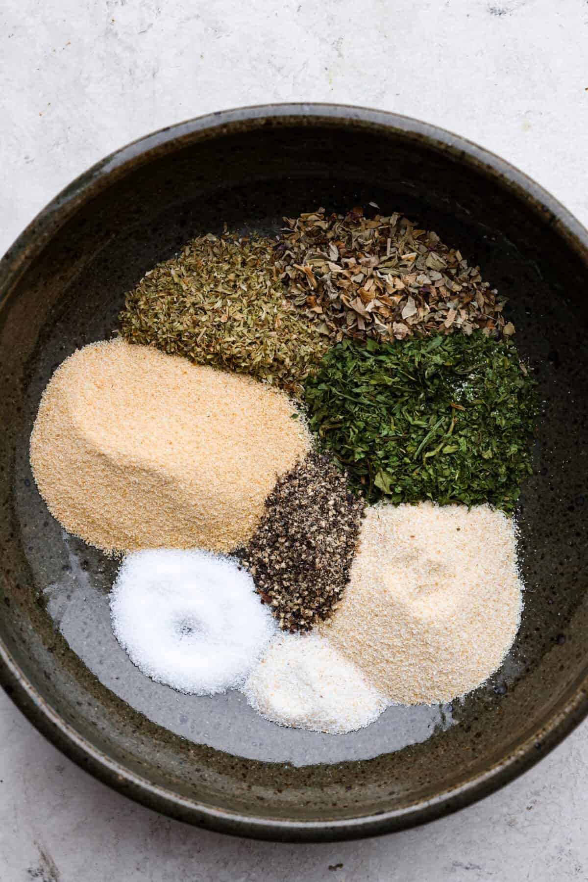 Homemade garlic herb seasoning is a great mix to have on hand. It has multiple uses, is full of flavor, and is adjustable to suit your taste preferences. It has the perfect mix of herbaceous dried herbs, garlic, onion powder, salt, and fresh cracked pepper. Overhead shot of each ingredient for homemade garlic herb seasoning in the same bowl in separate piles.
