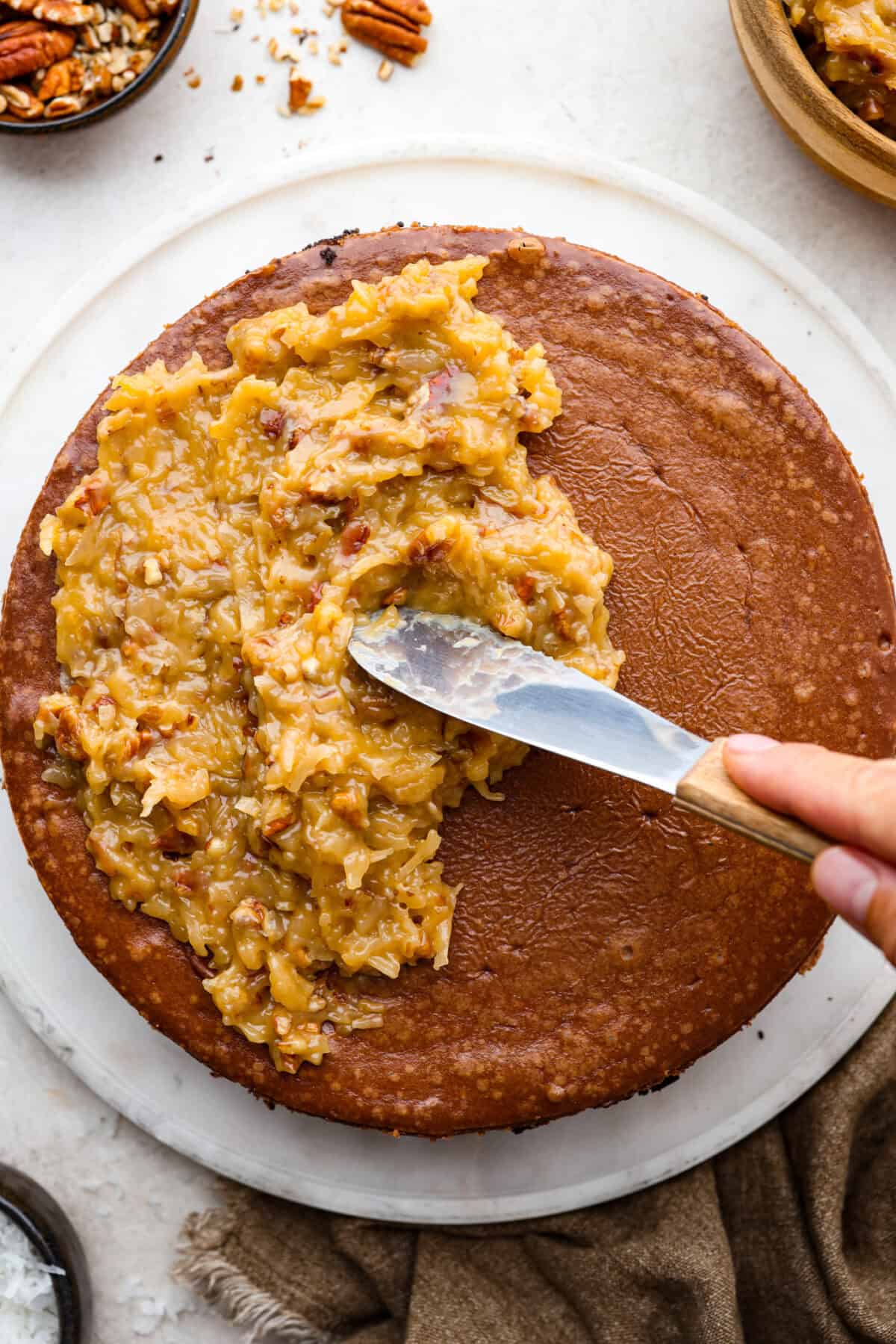 German Chocolate Cheesecake is a rich and impressive dessert! It has an Oreo cookie crust, a chocolate cheesecake filling, and a classic German chocolate topping to finish it off! The gooey coconut pecan topping takes this cheesecake to the next level! Top close view of the German topping spreading on top of the German Chocolate cheesecake.