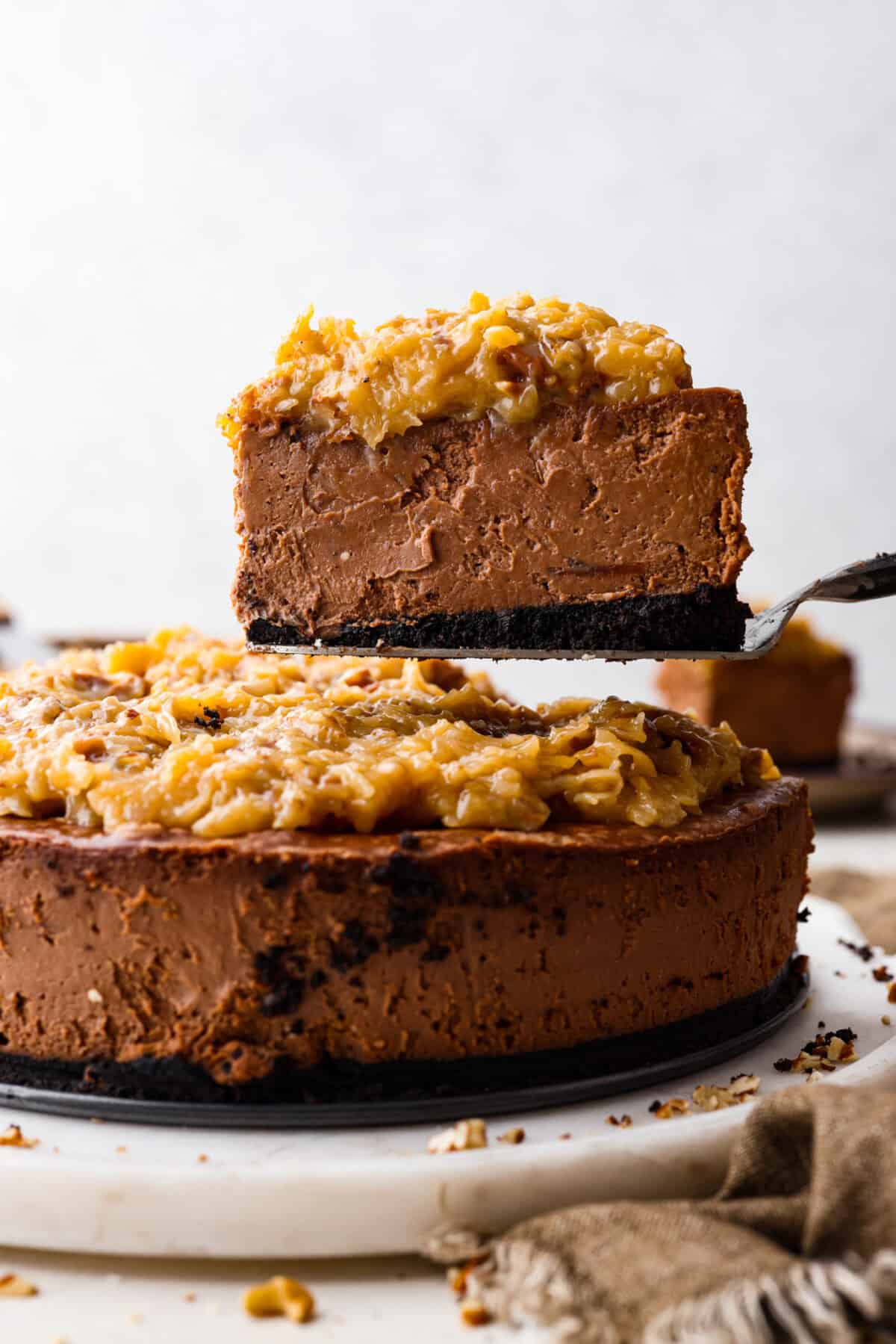German Chocolate Cheesecake is a rich and impressive dessert! It has an Oreo cookie crust, a chocolate cheesecake filling, and a classic German chocolate topping to finish it off! The gooey coconut pecan topping takes this cheesecake to the next level! Close side view of a slice of German chocolate cheesecake on a serving spatula.