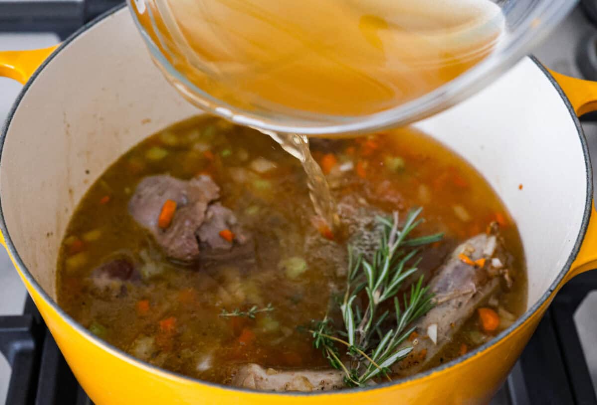 Giblet gravy is a labor of love, but the flavor is unmatched! Using the turkey's neck, gizzard, heart, liver, and drippings, you can make the best gravy you've ever had! It will be the perfect complement to your holiday turkey dinner. Angle shot of someone pouring chicken broth into the pot with giblets, vegetables, garlic and sprigs of fresh herbs.