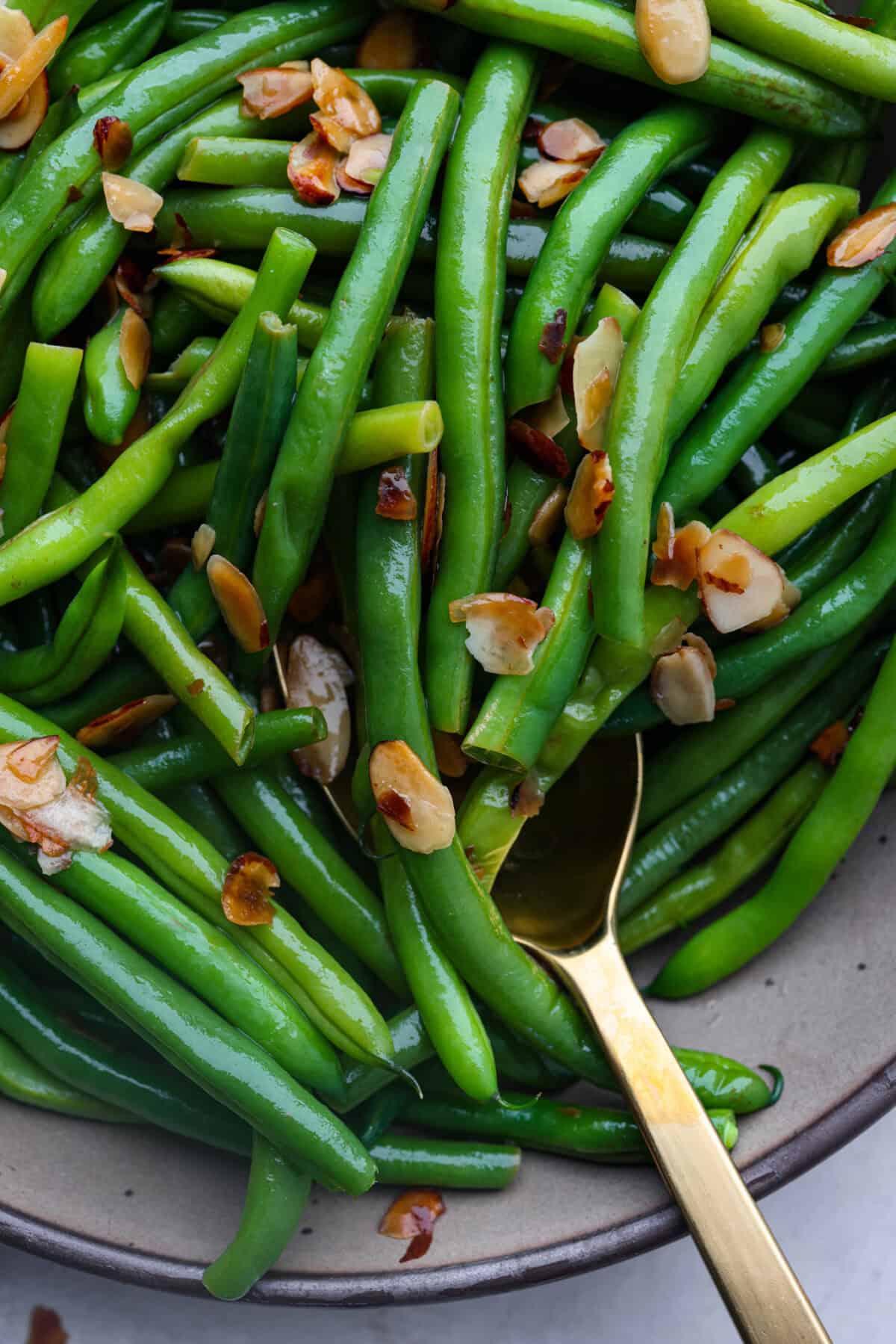 Green Beans Almondine is made with fresh green beans that are sautรฉed until crisp-tender and then tossed with buttery, toasted almonds. Every bite is filled with nutty richness and a hint of lemon to brighten up the flavors. Close up shot of green beans Almondine.