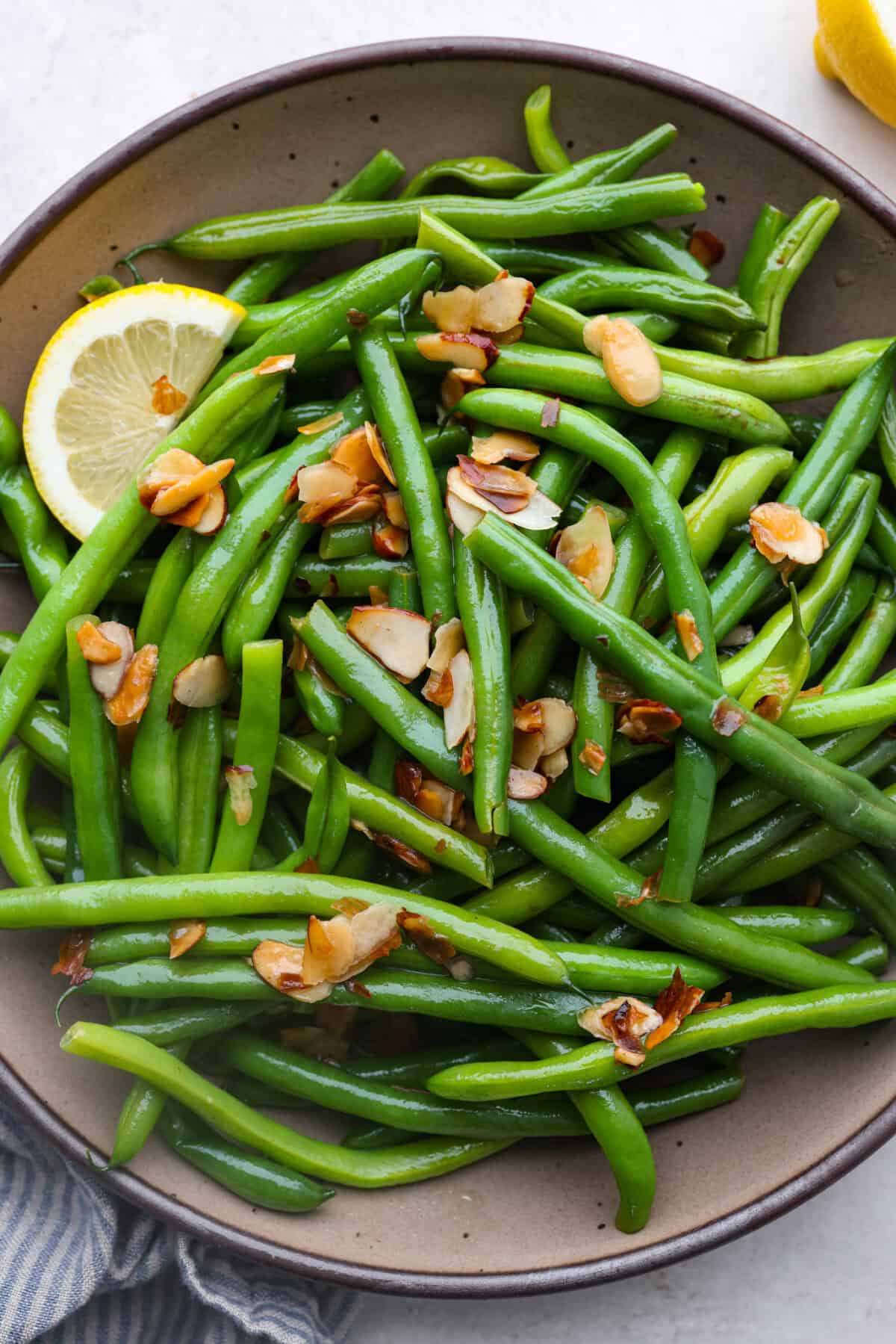 Green Beans Almondine is made with fresh green beans that are sautรฉed until crisp-tender and then tossed with buttery, toasted almonds. Every bite is filled with nutty richness and a hint of lemon to brighten up the flavors. Overhead shot of green beans Almondine in a serving platter.