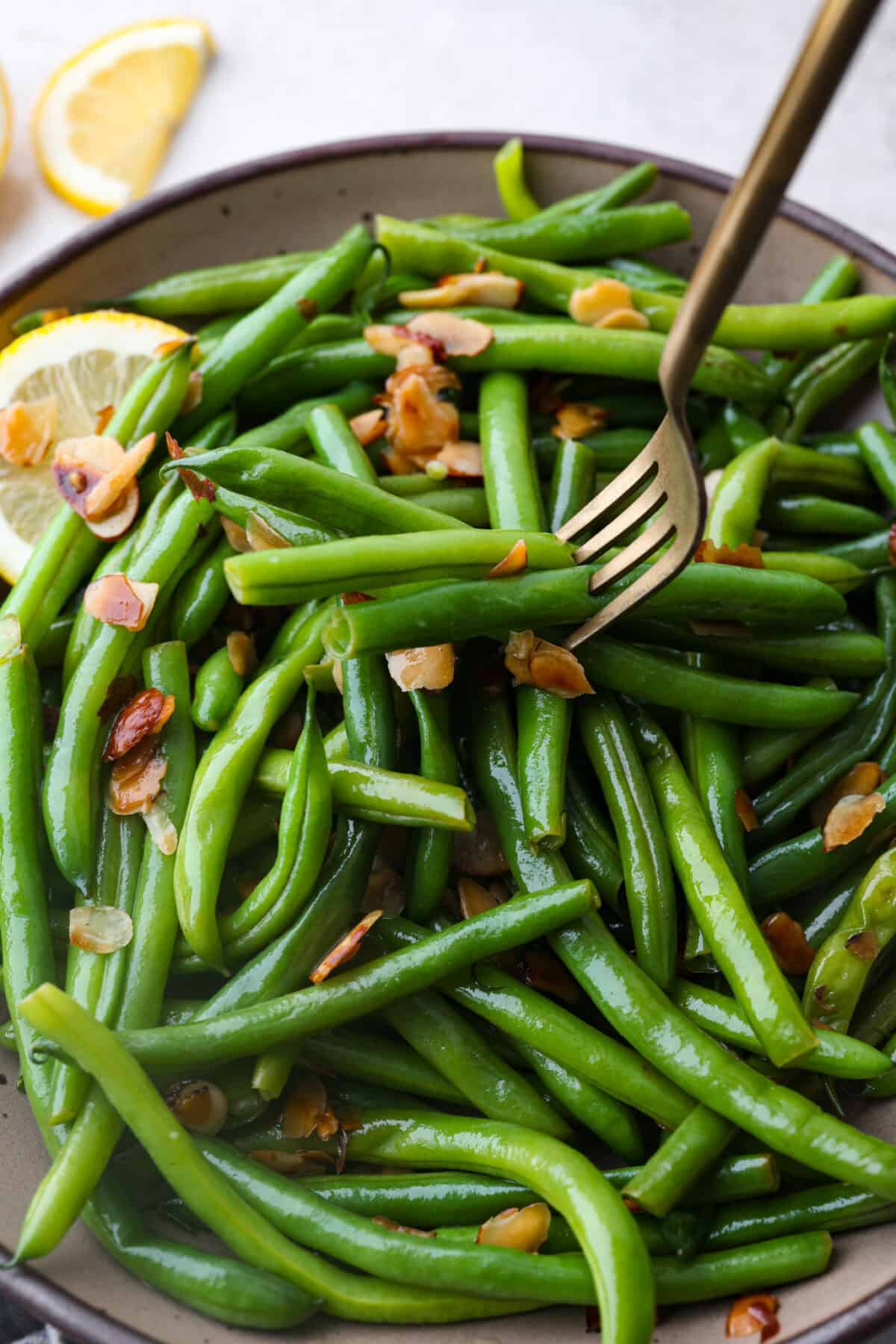 Green Beans Almondine is made with fresh green beans that are sautรฉed until crisp-tender and then tossed with buttery, toasted almonds. Every bite is filled with nutty richness and a hint of lemon to brighten up the flavors. Angle shot of green beans Almondine with a fork spearing some of the beans.