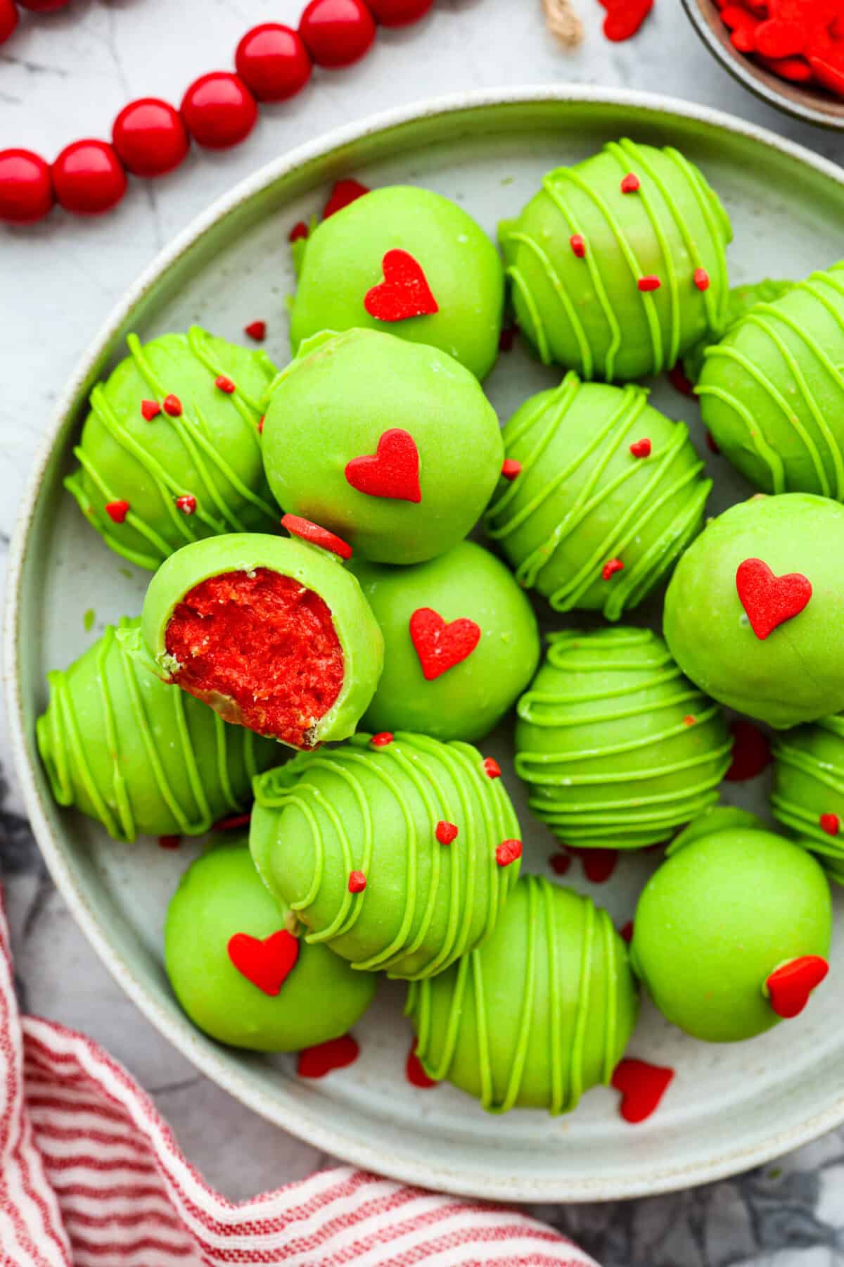 These are the cutest Grinch Oreo balls you have ever seen! Fudgy Oreo filling is coated in green candy melts and garnished with the cutest red heart sprinkle. They taste amazing and will steal the show this holiday season at holiday parties, family get-togethers, or Christmas events. Overhead shot of Grinch Oreo balls on a serving platter.