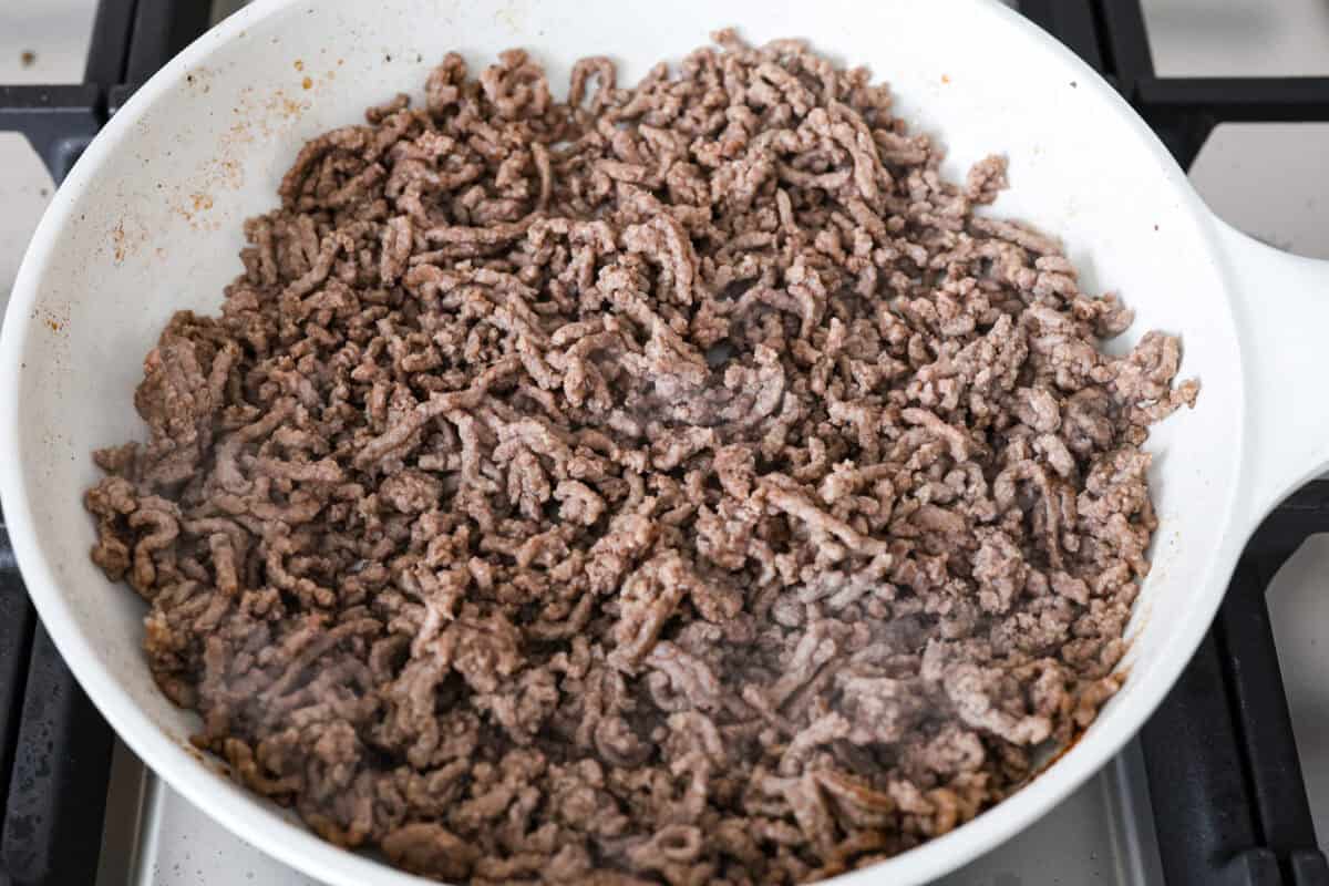 Enjoy delicious Asian flavors in these Korean Beef Lettuce Wraps! This appetizer or main is loaded with tasty lean ground beef, sautรฉed shredded carrots, red bell pepper, and garlic, all tossed in a mouthwatering sauce and spooned into lettuce leaves. Overhead shot of beef browning in a skillet.
