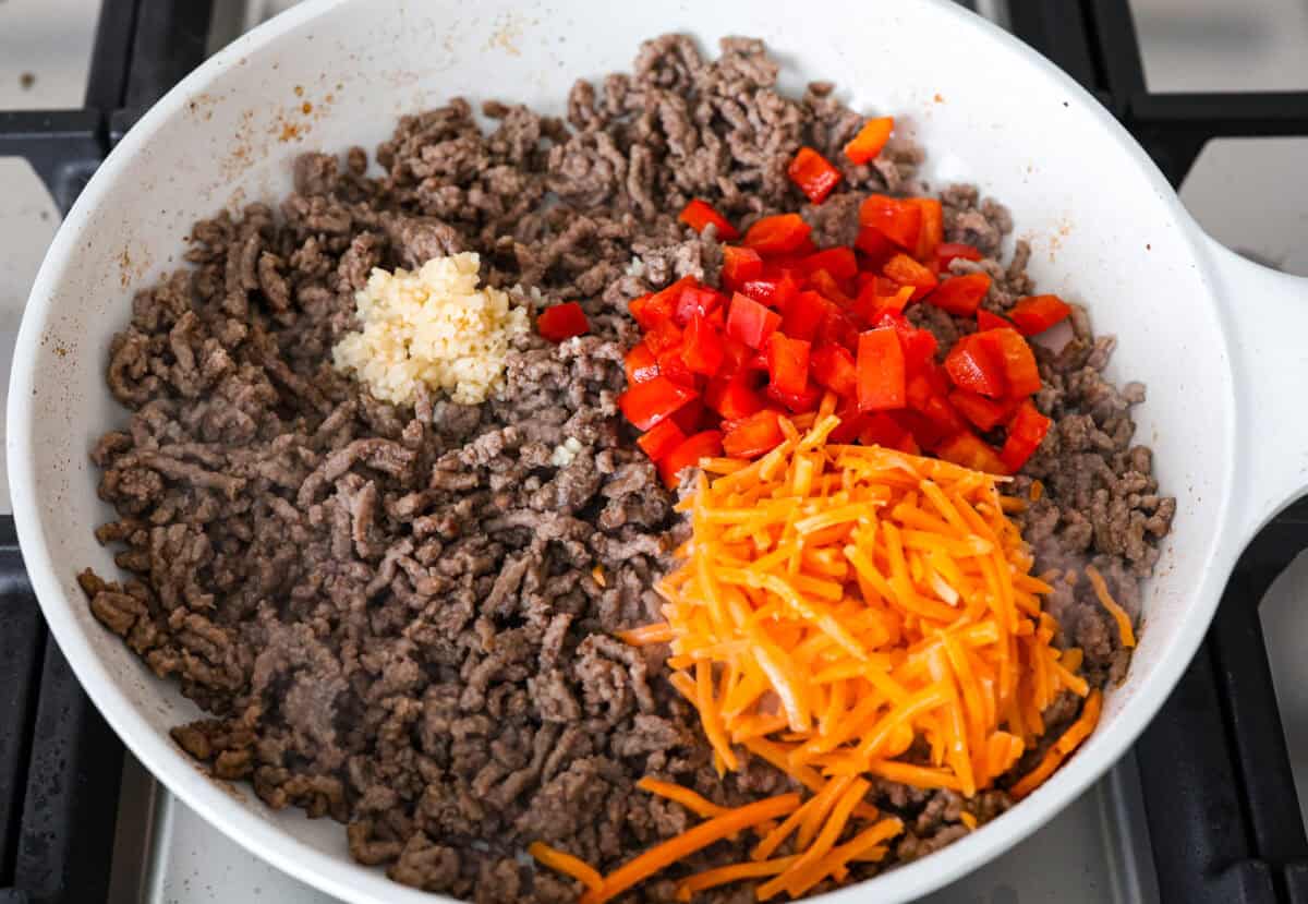 Enjoy delicious Asian flavors in these Korean Beef Lettuce Wraps! This appetizer or main is loaded with tasty lean ground beef, sautรฉed shredded carrots, red bell pepper, and garlic, all tossed in a mouthwatering sauce and spooned into lettuce leaves. Overhead shot of browned beef with carrot shreds, red pepper and garlic on top.