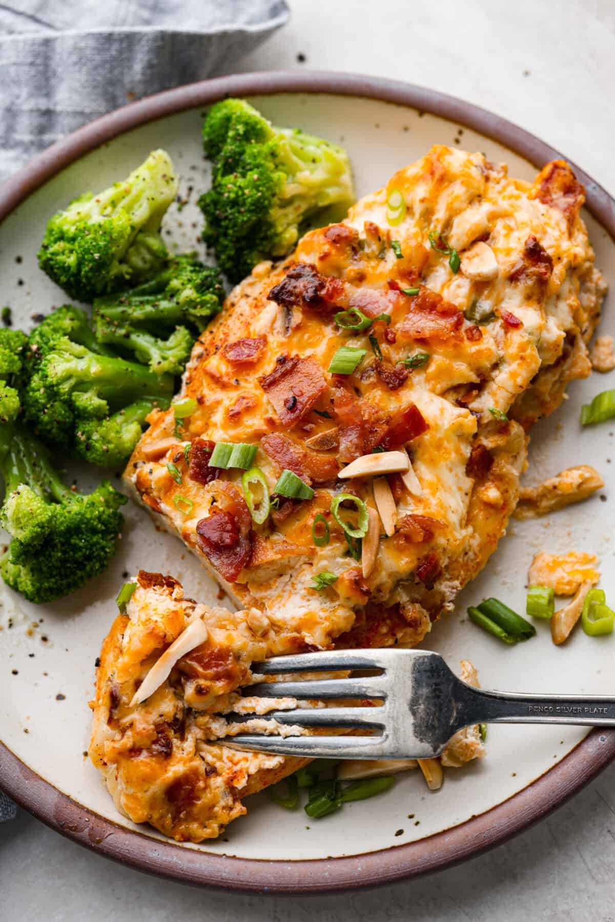 Million Dollar Chicken features juicy baked chicken topped with a creamy, cheesy layer that’s bursting with flavor. The crispy bacon and crunchy almonds really take this to the next level. Enjoy with rice, pasta, vegetables, or any of your favorite sides! Overhead shot of plated million dollar chicken with a side of broccoli.