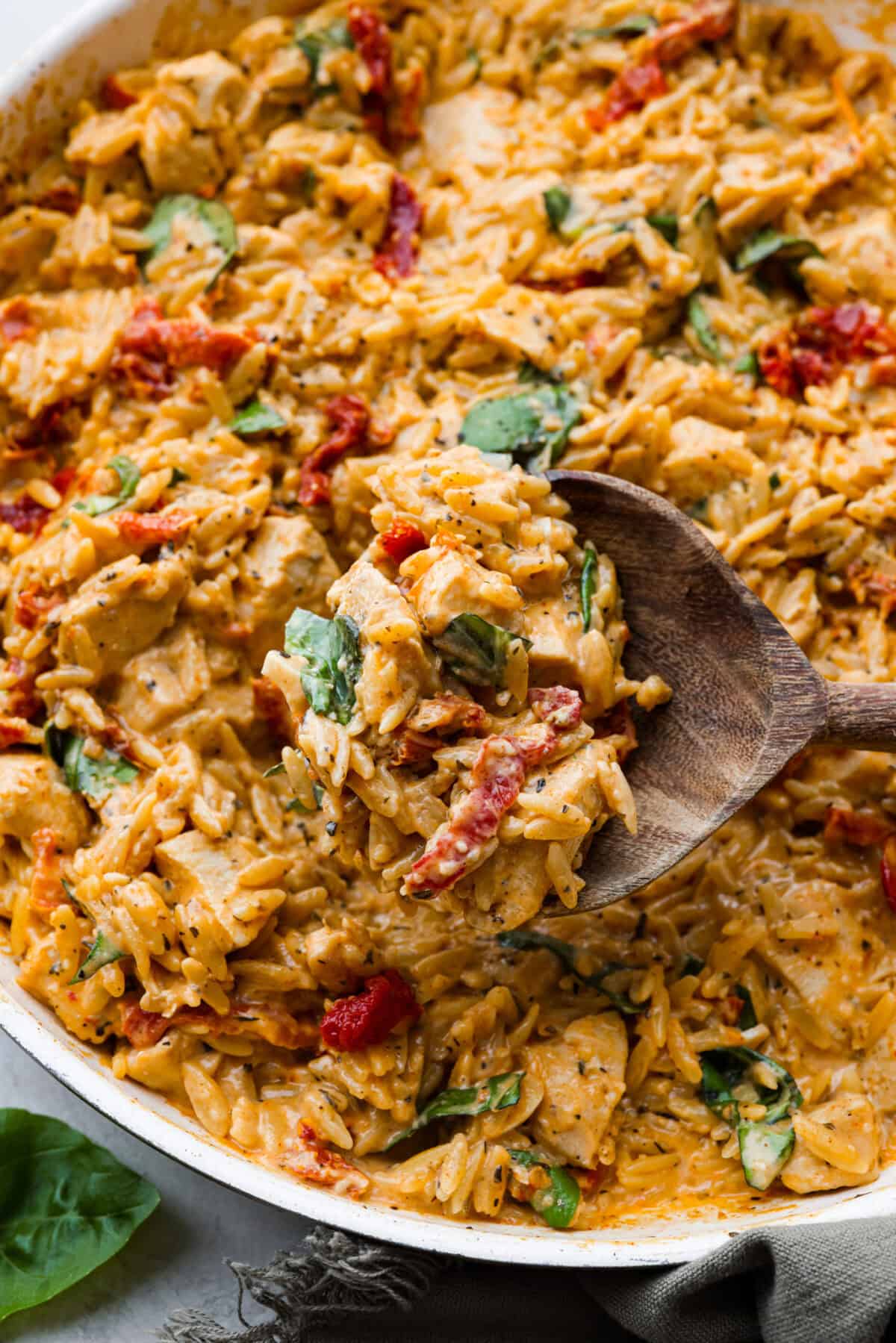 Win everyone over with One-Pan Marry Me Chicken Orzo! The recipe features tender chicken breasts cooked with orzo pasta in the most irresistible, creamy, sun-dried tomato sauce. It's quick to make and never disappoints! Close up shot of a scoop of marry me chicken orzo being taken out of the pan.