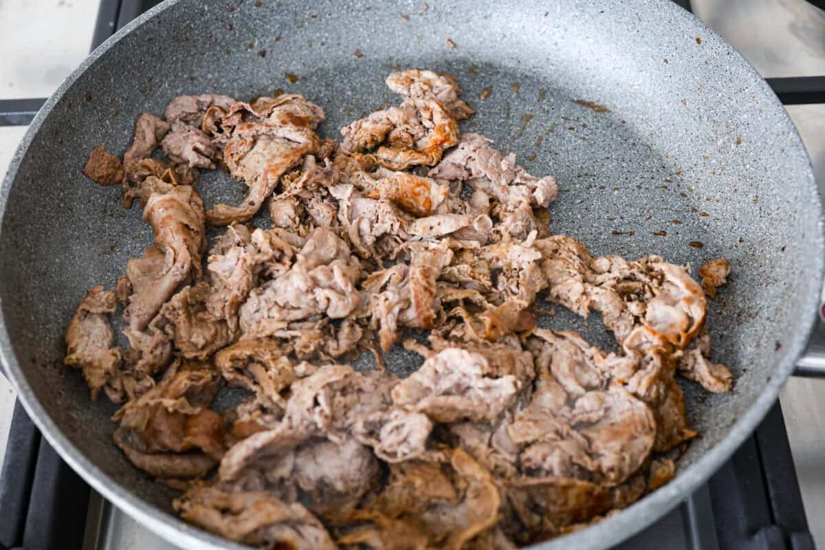 Philly cheesesteak sliders are a fun and delicious twist on a classic. These Philly cheesesteaks are filled with thinly sliced steak, caramelized onions, crisp peppers, and, of course, melty cheese. Overhead shot of beef cooking in a skillet.