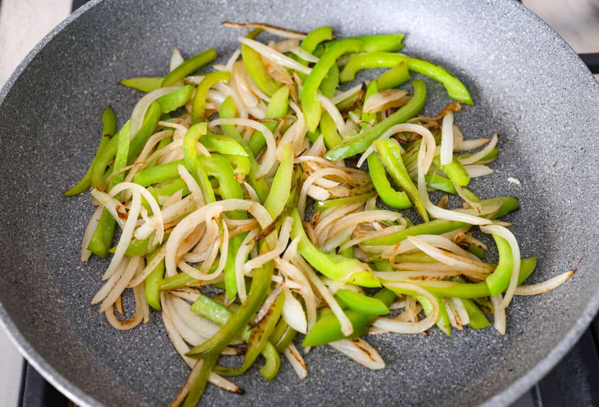 Philly cheesesteak sliders are a fun and delicious twist on a classic. These Philly cheesesteaks are filled with thinly sliced steak, caramelized onions, crisp peppers, and, of course, melty cheese. Overhead shot of onions and green peppers cooking in a skillet.