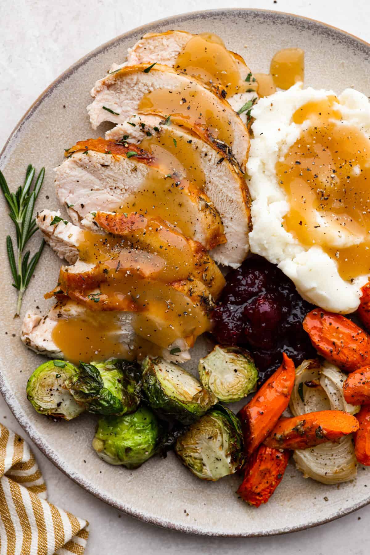Look no further! This roasted turkey recipe is the absolute juiciest, fool-proof turkey recipe you will ever need. You'll have the confidence to make a perfect turkey every time. This deliciously seasoned turkey will be the star of your Thanksgiving meal! Top view of Thanksgiving dinner and oven roasted turkey on a plate.