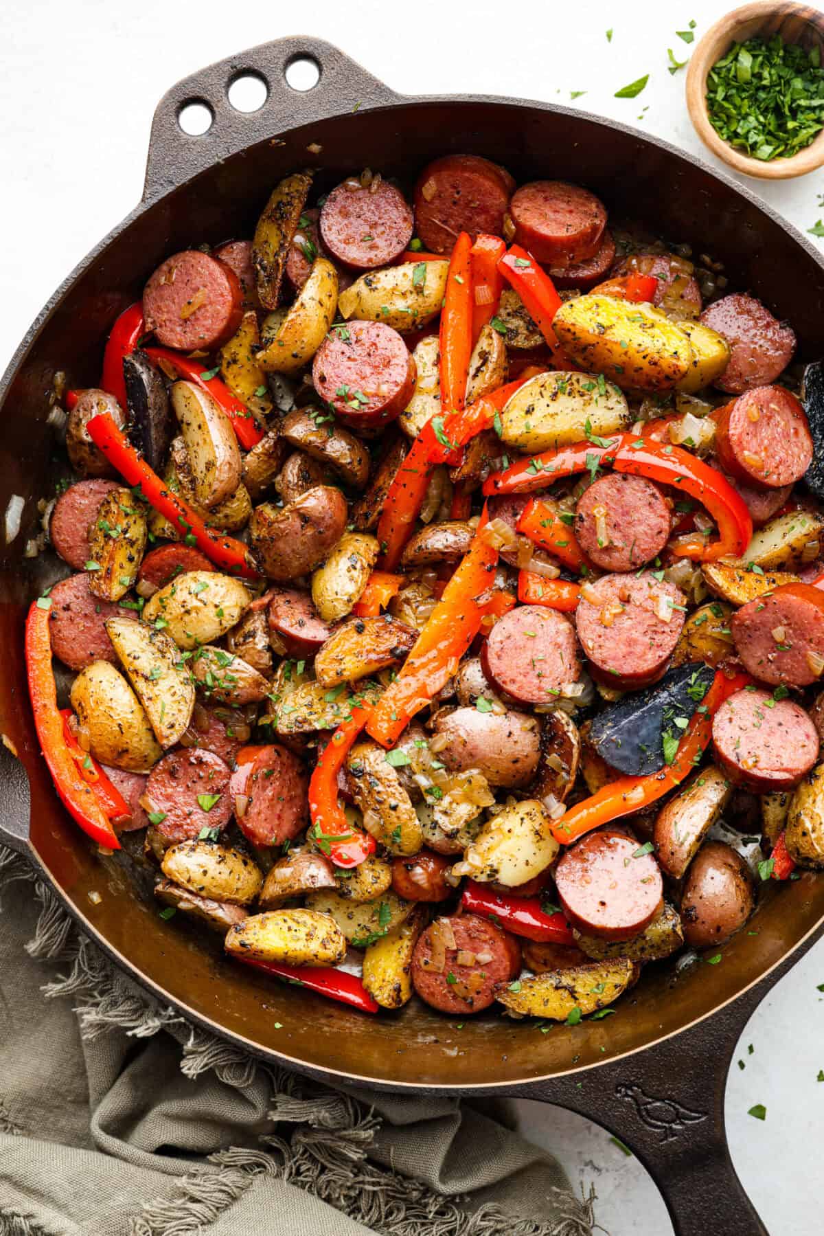 This sausage and potato skillet recipe is meant to be a simple one skillet meal! It has tender baby potatoes, smoked sausage, peppers, and delicious seasonings that take it over the top. It's hearty, satisfying and loaded with flavor! Top view of sausage and potato skillet in a cast iron skillet.