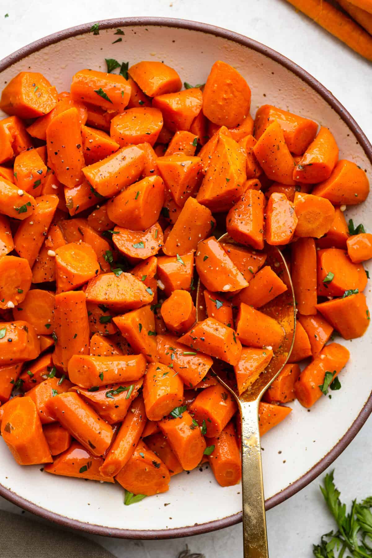 These crockpot carrots will become fork-tender from slowly cooking in your crockpot all day. The carrots have a delicious sweet and savory flavor from the sticky honey and bold garlic, all slathered in butter. They are the perfect side for your next Thanksgiving or Easter feast. Overhead shot of crockpot carrots on a serving platter.