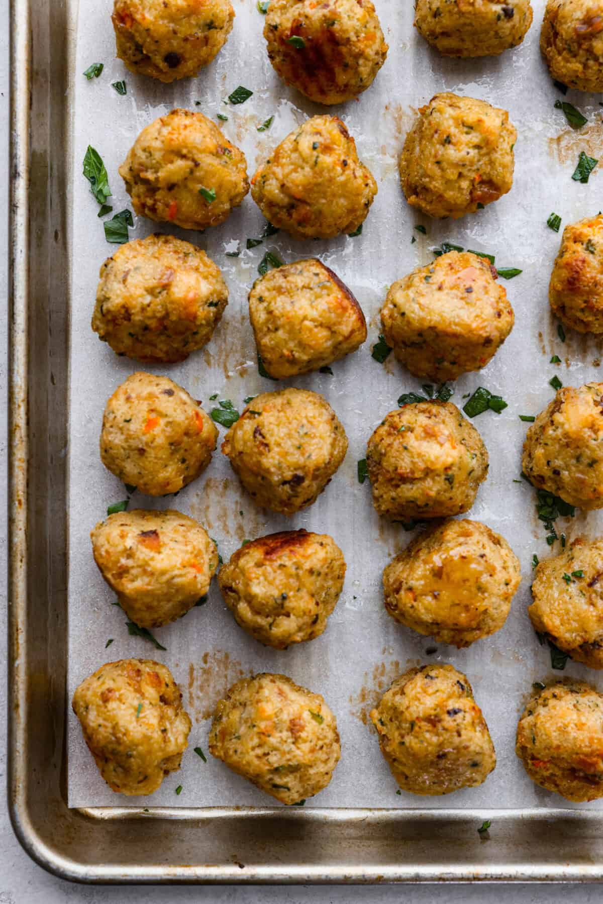 Turkey Stuffing Balls capture the taste of Thanksgiving in a single bite! Made with tender turkey, flavorful stuffing, and mashed potatoes. Theyโre rolled into perfectly poppable bites and served with rich gravy for dipping. Overhead shot of cooked turkey stuffing balls on parchment paper on a cookie sheet.