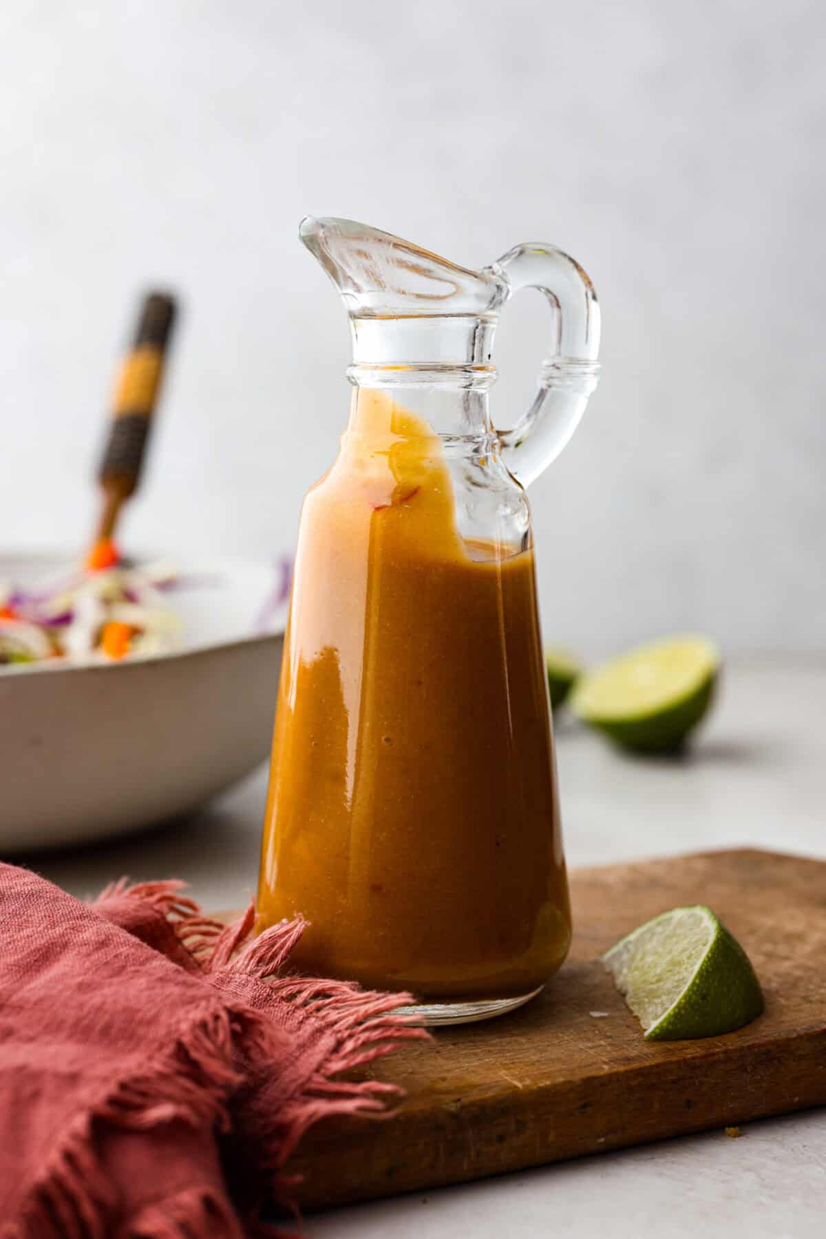 Thai peanut dressing is perfect for drizzling over fresh chopped salads or dipping veggies. It's a creamy mix of peanut butter, soy sauce, lime juice, and sweet chili sauce with a touch of garlic and ginger. Itโs nutty and tangy, with the perfect amount of spice. Side shot of Thai peanut dressing in a glass container.