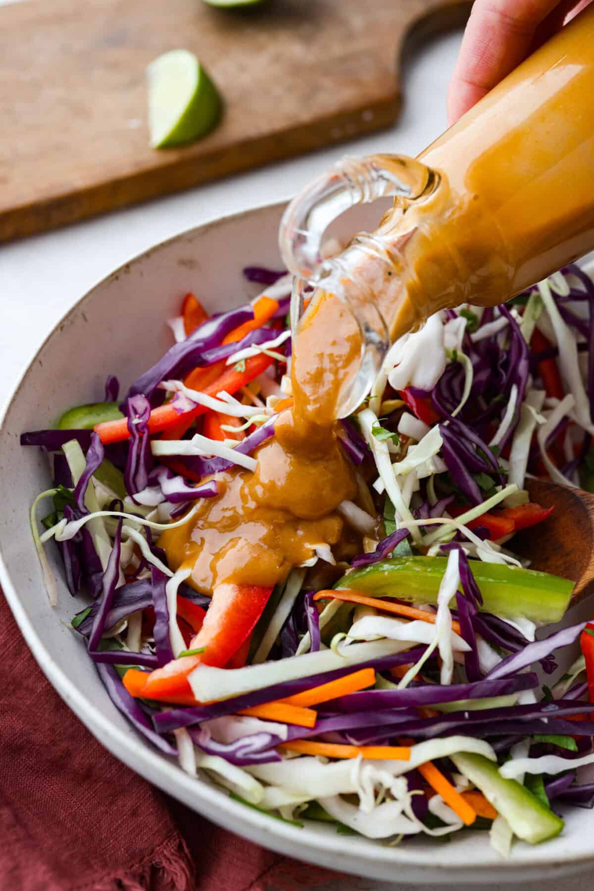 Thai peanut dressing is perfect for drizzling over fresh chopped salads or dipping veggies. It's a creamy mix of peanut butter, soy sauce, lime juice, and sweet chili sauce with a touch of garlic and ginger. Itโs nutty and tangy, with the perfect amount of spice. Angle shot of Thai peanut dressing being drizzled over salad.