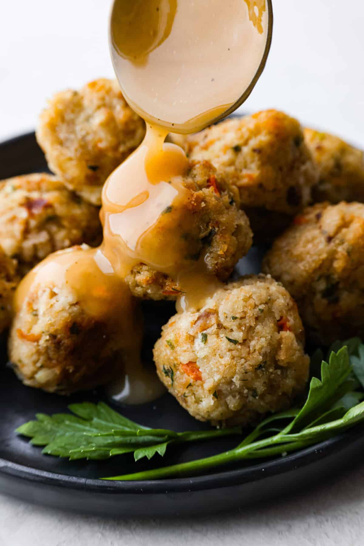 Turkey Stuffing Balls capture the taste of Thanksgiving in a single bite! Made with tender turkey, flavorful stuffing, and mashed potatoes. Theyโre rolled into perfectly poppable bites and served with rich gravy for dipping. Close up shot of someone pouring gravy over turkey stuffing balls.