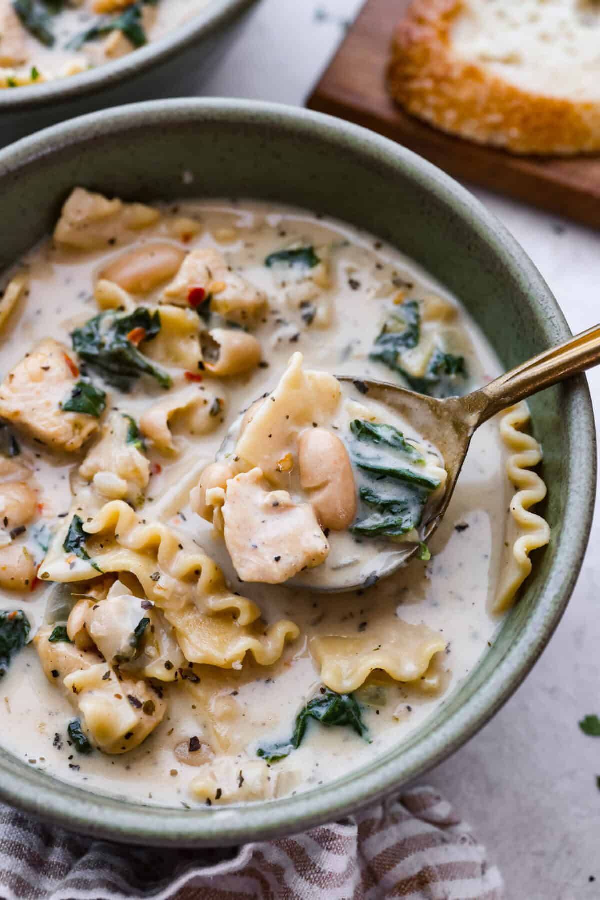 Comforting White Lasagna Soup is warm, creamy, and packed with rich flavors. With its hearty mix of chicken, noodles, white beans, and cheese, it’s a guaranteed crowd-pleaser. Deconstructed white lasagna in a satisfying soup! Close up shot of a bowl of white lasagna soup with a spoon lifting a bite out.