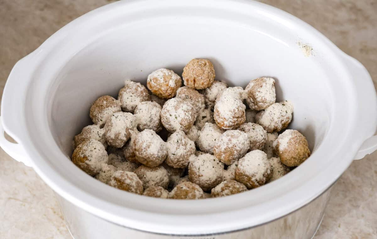 Crockpot Mississippi meatballs make the best little appetizer or side dish. The flavorful pepperoncini mixed with the au jus and ranch seasoning packets with delectable butter makes the most amazing sauce. It's perfectly soaked up by the tender meatballs. Angle shot of frozen meatballs with seasoning packets sprinkled over the top in a crockpot.