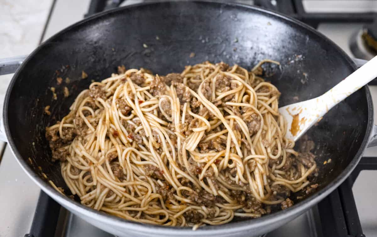 Mongolian Ground Beef and Noodles is a flavorful dinner that’s ready in 30 minutes! This dish combines tender noodles, savory ground beef, and a sweet and tangy Asian-inspired sauce for a meal that’s as comforting as it is delicious! Angle shot of everything being mixed together in a skillet.