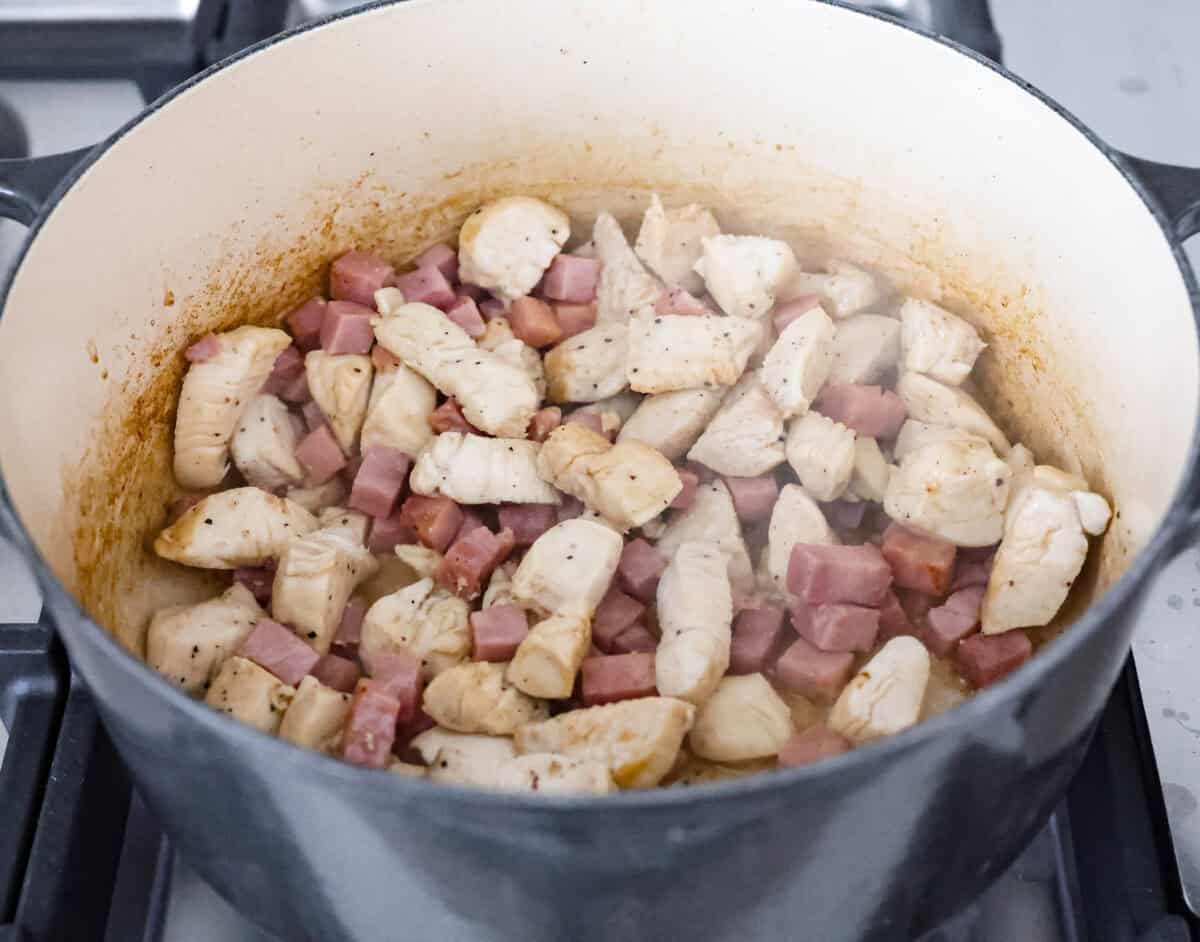 Chicken cordon bleu pasta is a creamy, flavorful dish that's a fun twist on the classic. It combines savory ham, tender chicken, melty cheese, and delicious seasonings. Easy to make and sure to please! Angle shot of chicken and ham cooking in a pot.