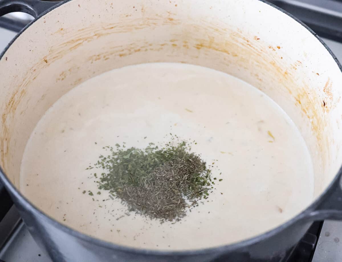 Chicken cordon bleu pasta is a creamy, flavorful dish that's a fun twist on the classic. It combines savory ham, tender chicken, melty cheese, and delicious seasonings. Easy to make and sure to please! Angle shot of seasonings on top of the sauce in a pot.