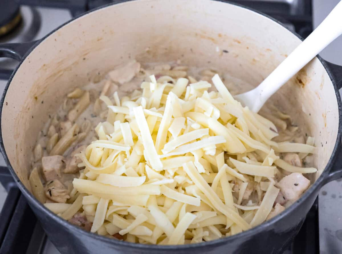 Chicken cordon bleu pasta is a creamy, flavorful dish that's a fun twist on the classic. It combines savory ham, tender chicken, melty cheese, and delicious seasonings. Easy to make and sure to please! Angle shot of cheese added to the chicken cordon bleu pasta in the pot.