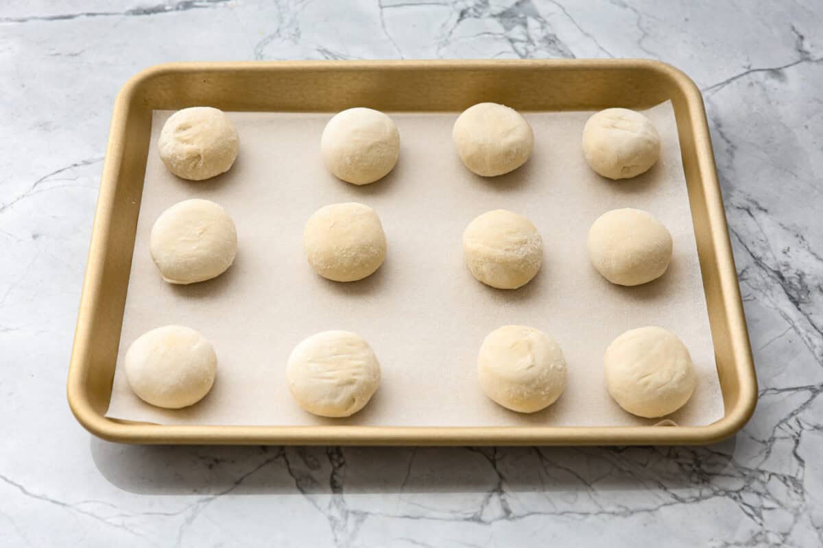 Irresistible Cinnamon Pull-Apart Bread is inspired by the popular cinnamon bread served at the Grist Mill eatery in Dollywood. With this copycat version, you can recreate that buttery, sweet deliciousness easily with frozen rolls. Angle shot of frozen dough balls on a cookie sheet.