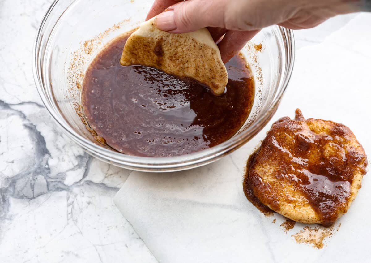 Irresistible Cinnamon Pull-Apart Bread is inspired by the popular cinnamon bread served at the Grist Mill eatery in Dollywood. With this copycat version, you can recreate that buttery, sweet deliciousness easily with frozen rolls. Angle shot of someone dipping the flattened dough into the butter, cinnamon and sugar mixture.