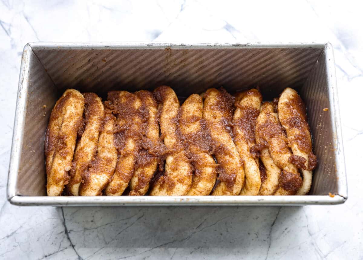 Irresistible Cinnamon Pull-Apart Bread is inspired by the popular cinnamon bread served at the Grist Mill eatery in Dollywood. With this copycat version, you can recreate that buttery, sweet deliciousness easily with frozen rolls. Overhead shot of the stack of dough balls on their side in a bread loaf pan.