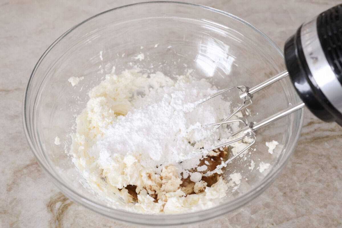 Starbucks copycat gingerbread loaf is the ultimate holiday treat! It's coated in a simple cream cheese frosting and is full of warm spices and rich molasses flavor. Enjoy it for Christmas brunch or a sweet treat at night! Overhead shot of someone using a hand mixer to mix the frosting ingredients together in a bowl.