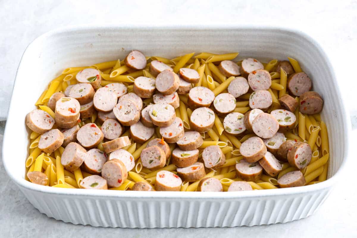 This one-pan Italian Sausage Casserole is the ultimate comfort food! With tender pasta, flavorful sausage, rich marinara, and gooey melted cheese, it’s an easy dinner that’s perfect for busy nights. It's a recipe the whole family will love! Angle shot of uncooked pasta with sausage over the top in the bottom of a baking dish.